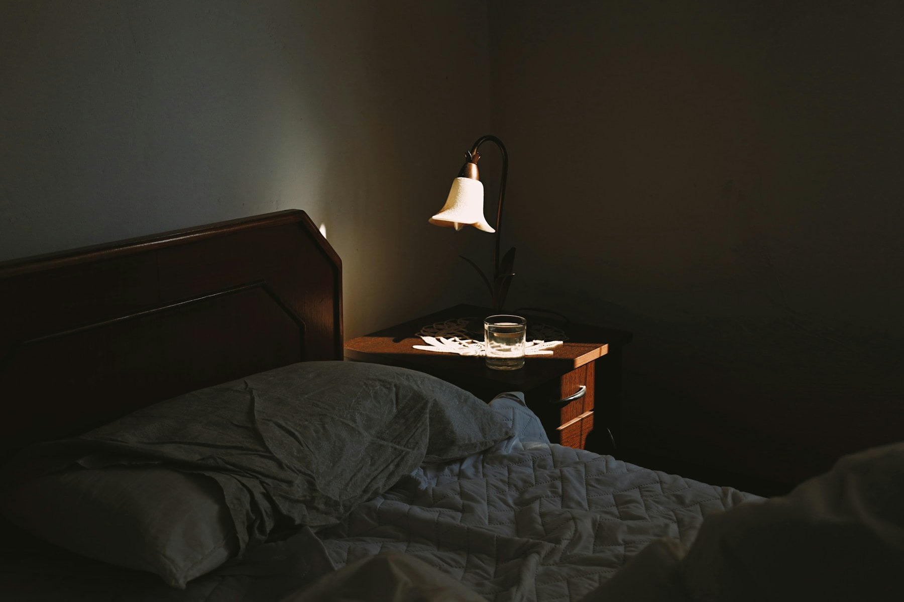 A softly lit bedside table with a lamp and water glass beside a bed