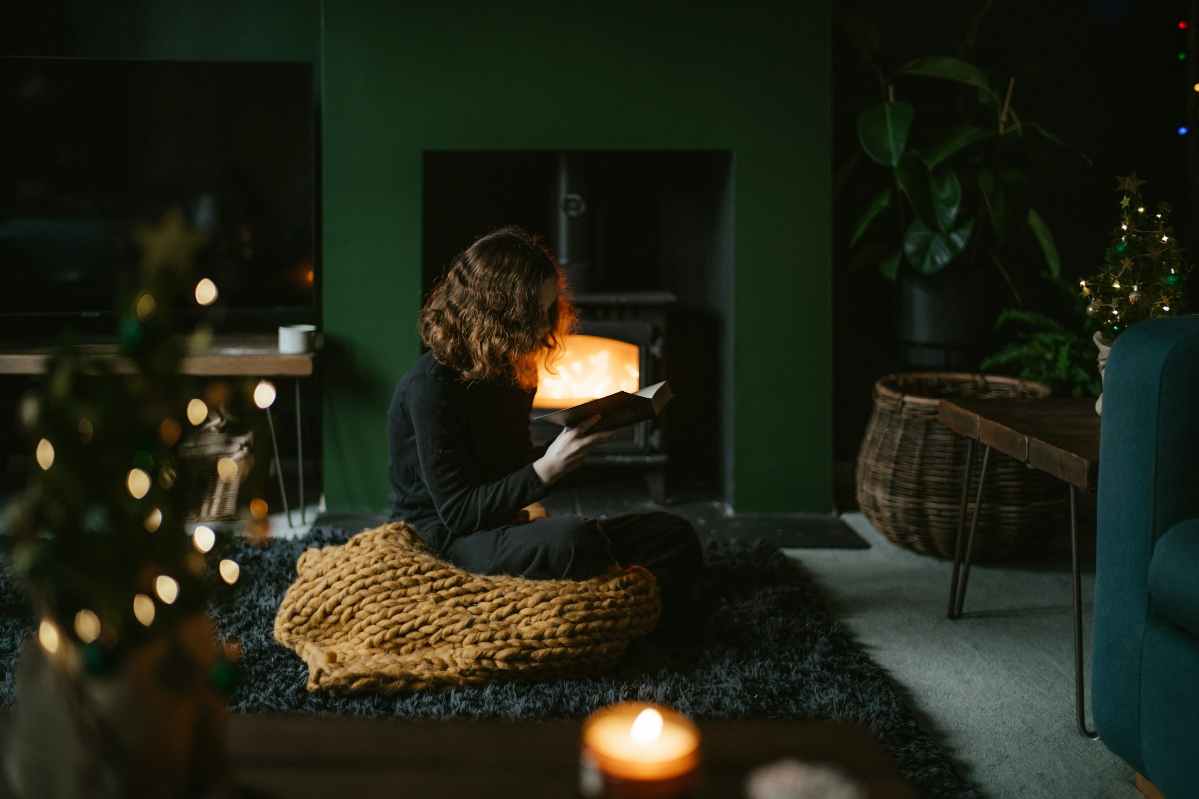 A person reading beside a fireplace in a quiet evening room