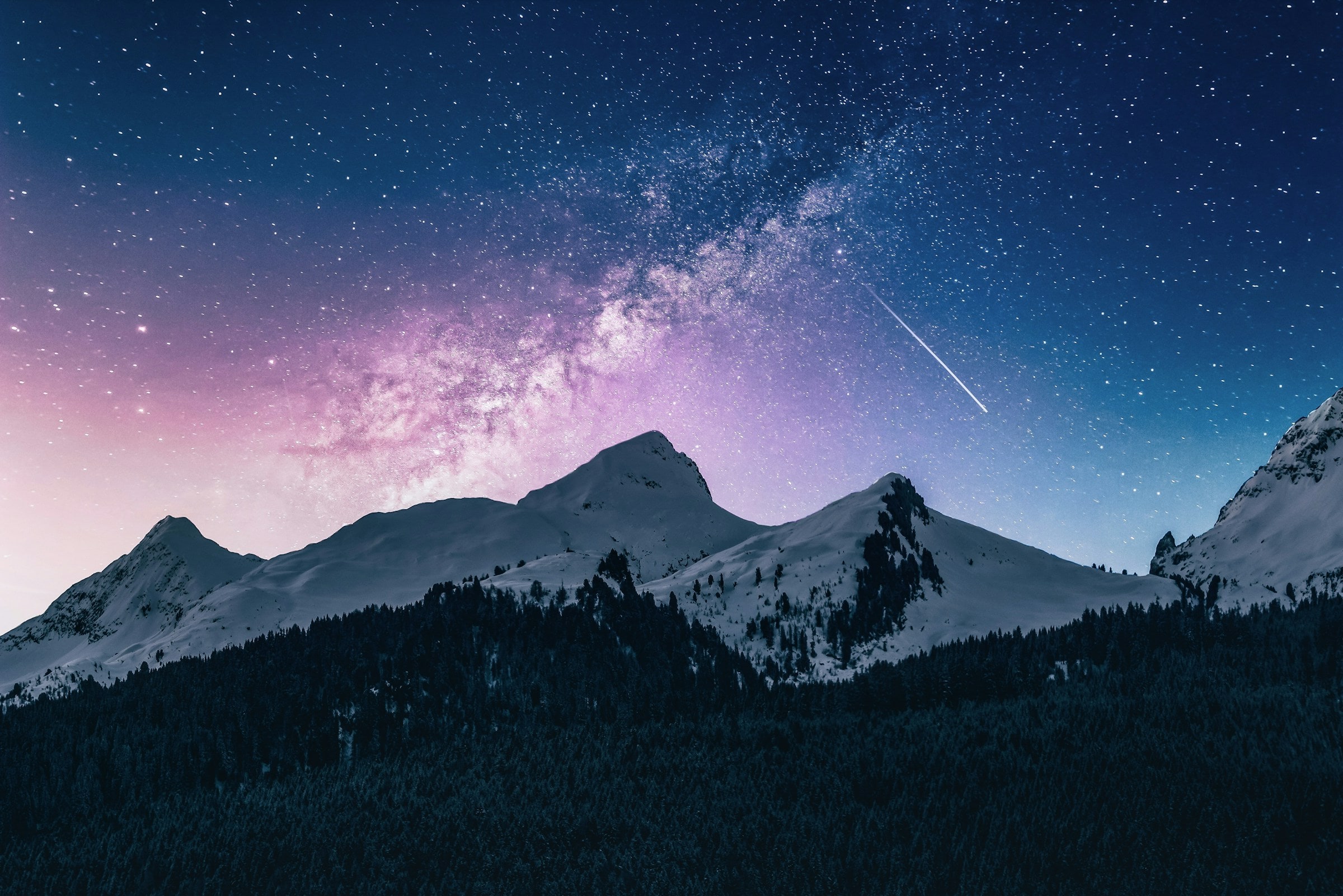 A star-filled night sky over snow-covered mountains