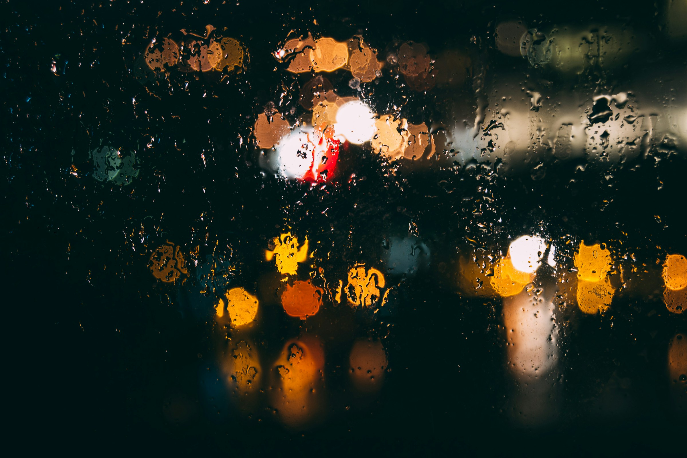 Rain drops on glass against softly glowing lights
