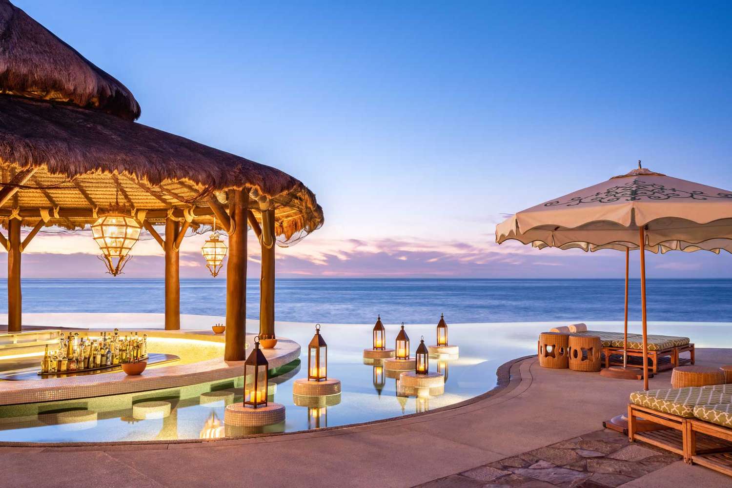 Oceanfront resort pool and lounge area at sunset in Los Cabos