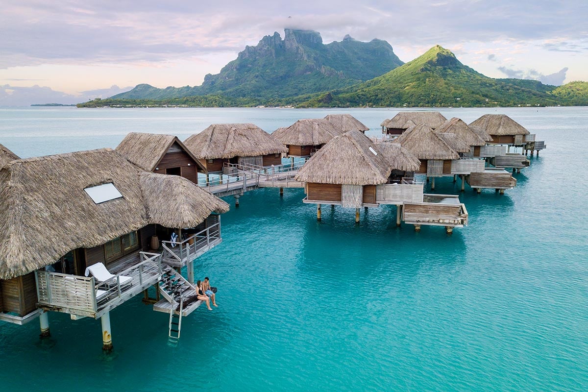 Overwater bungalows beside a turquoise lagoon and green mountain