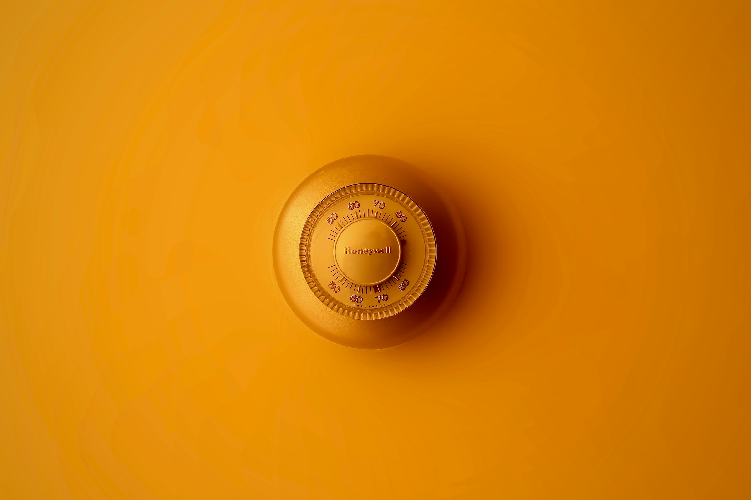 Round wall thermostat on a warm orange wall