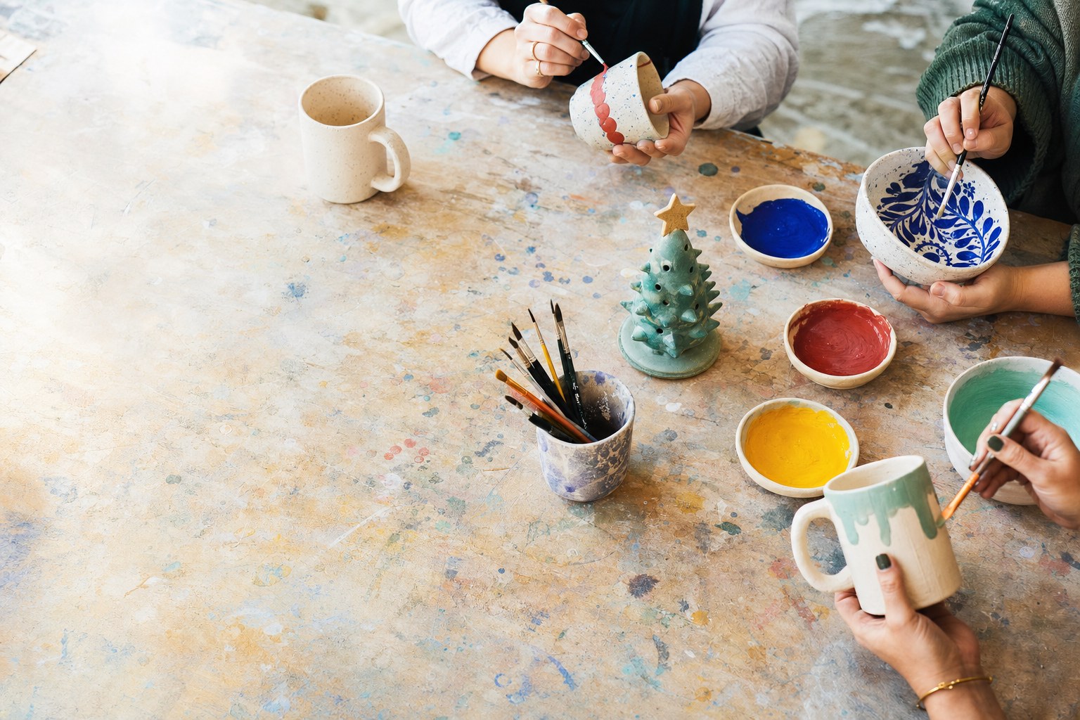 Hands painting handmade ceramic mugs and bowls at a studio table