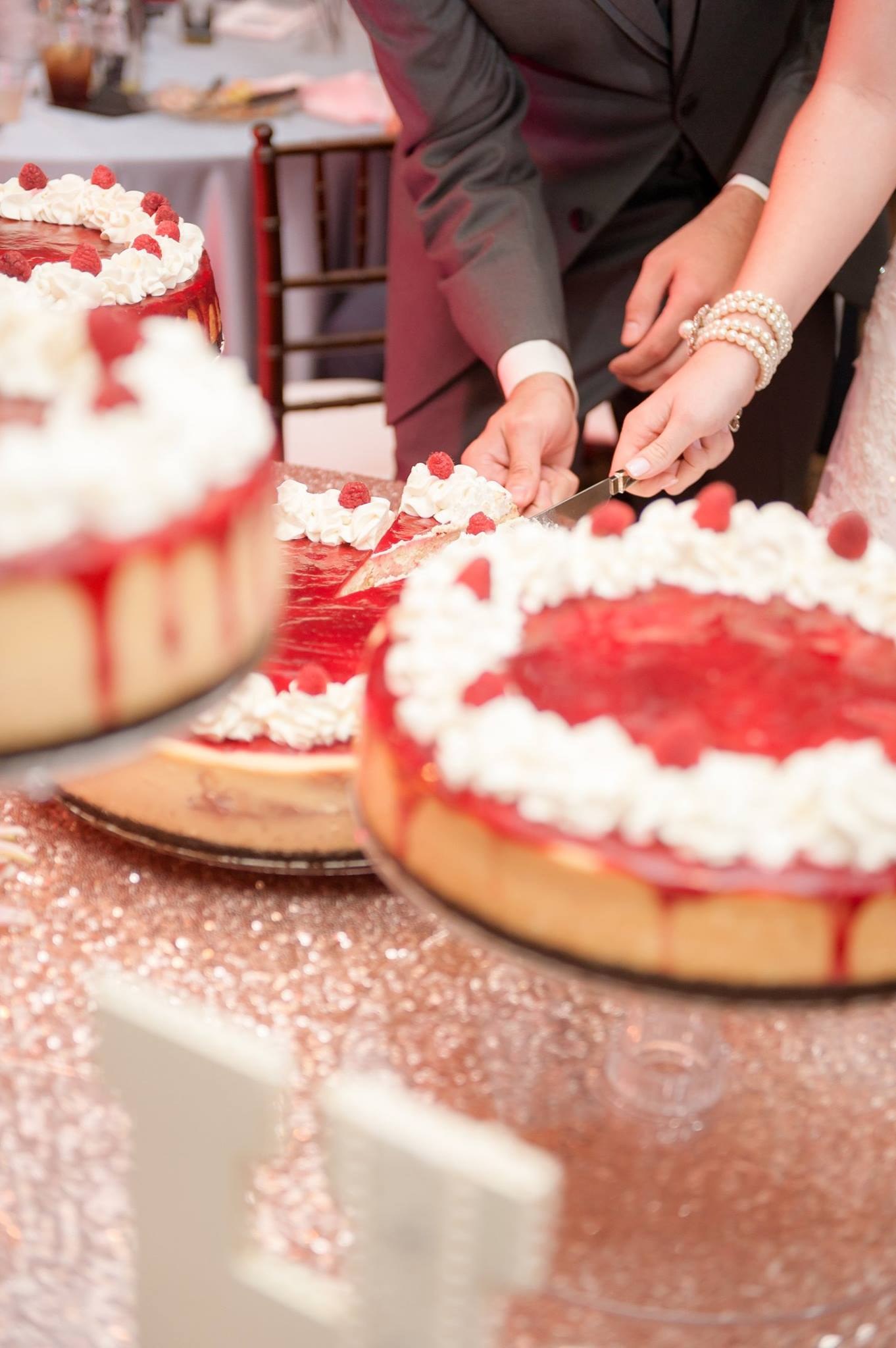 Couple cutting a raspberry-topped cheesecake at a wedding reception