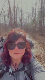Kristina wearing a backpack and sunglasses on a woodland trail