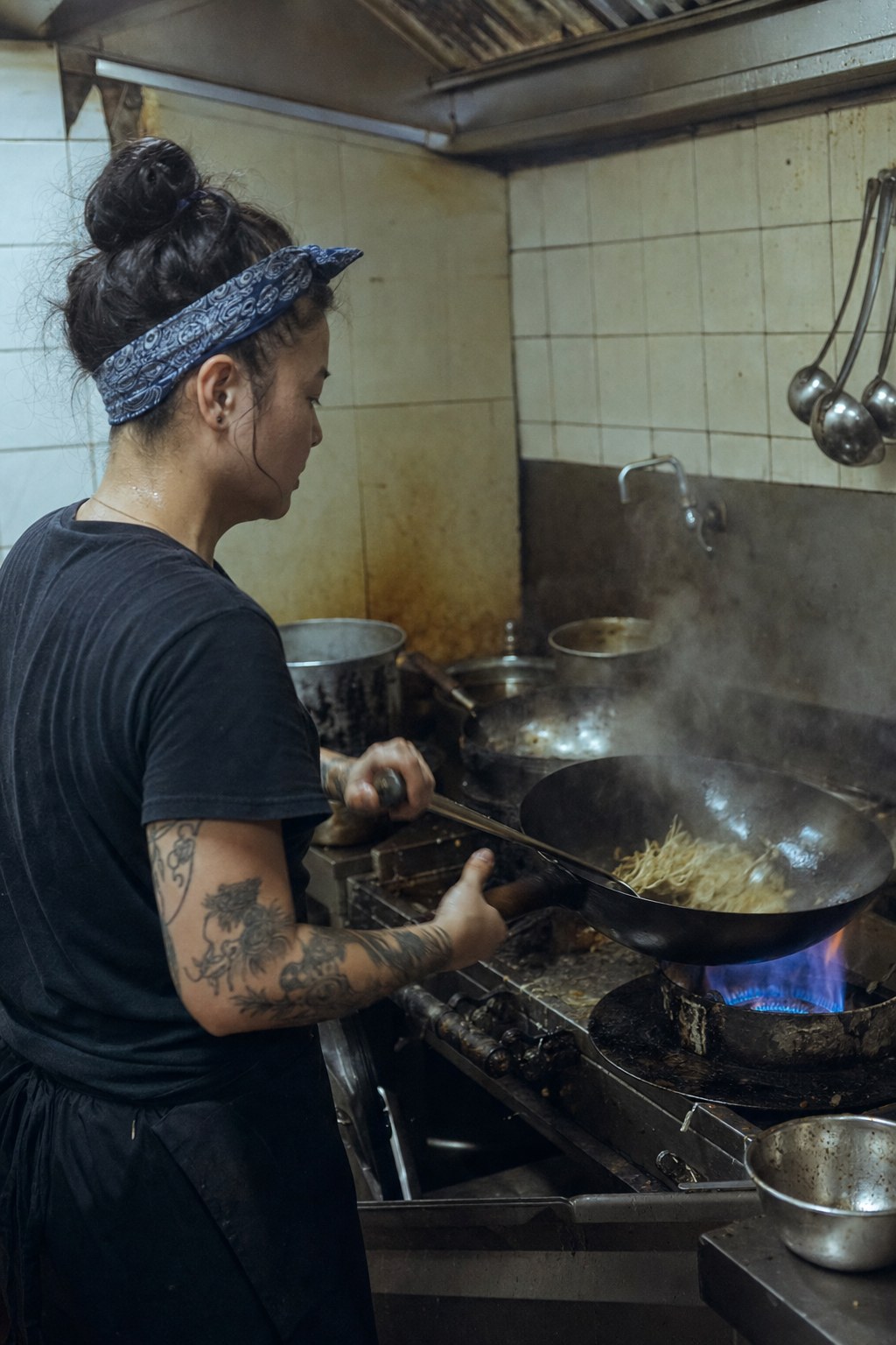 Woman cook working a hot wok station through the rush