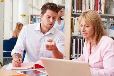 Two people reviewing notes and a laptop in a library