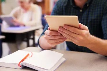 A learner using a tablet beside an open notebook