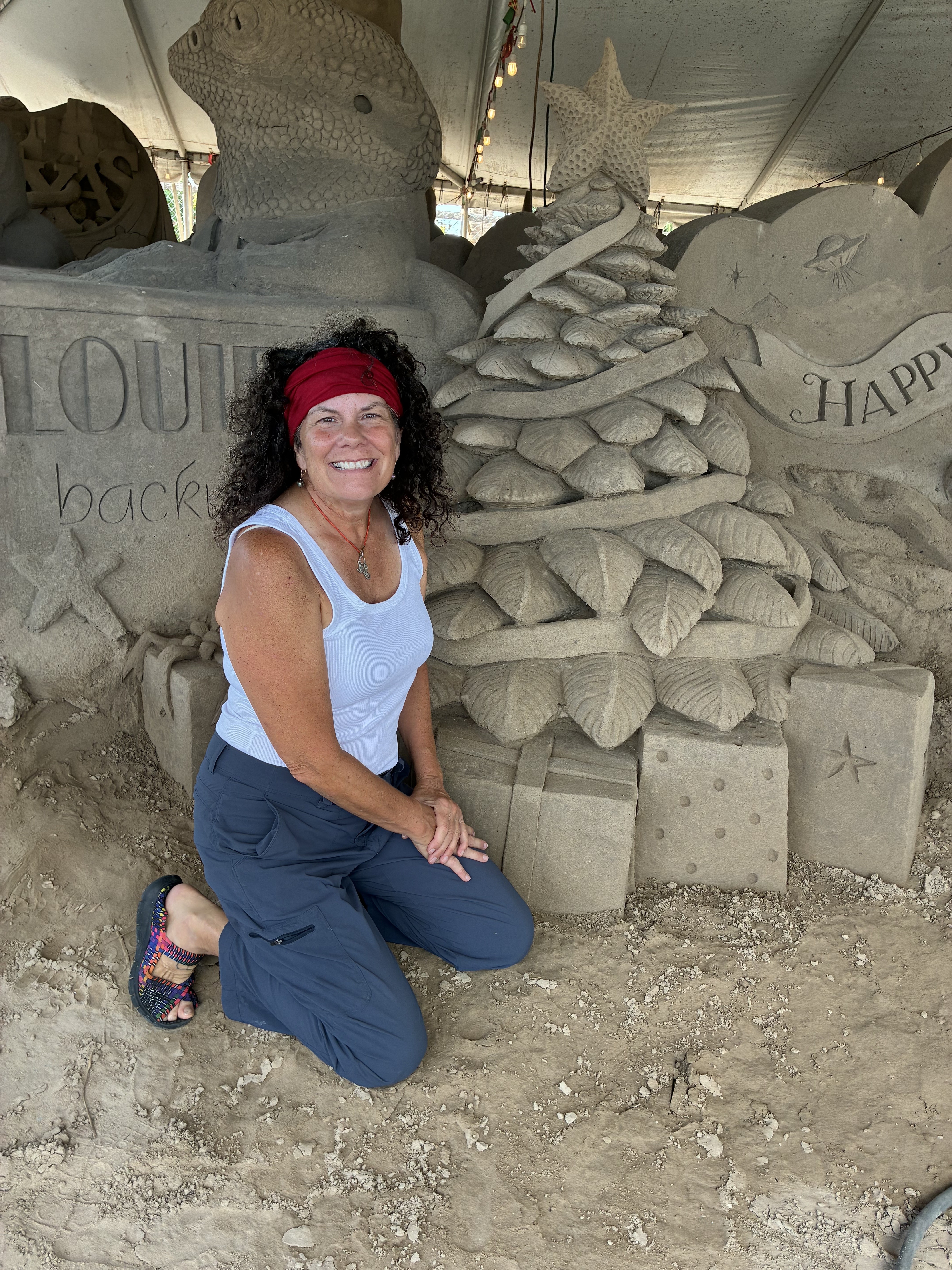 Janet Moore Schrader beside the sand Christmas tree and gifts she sculpted