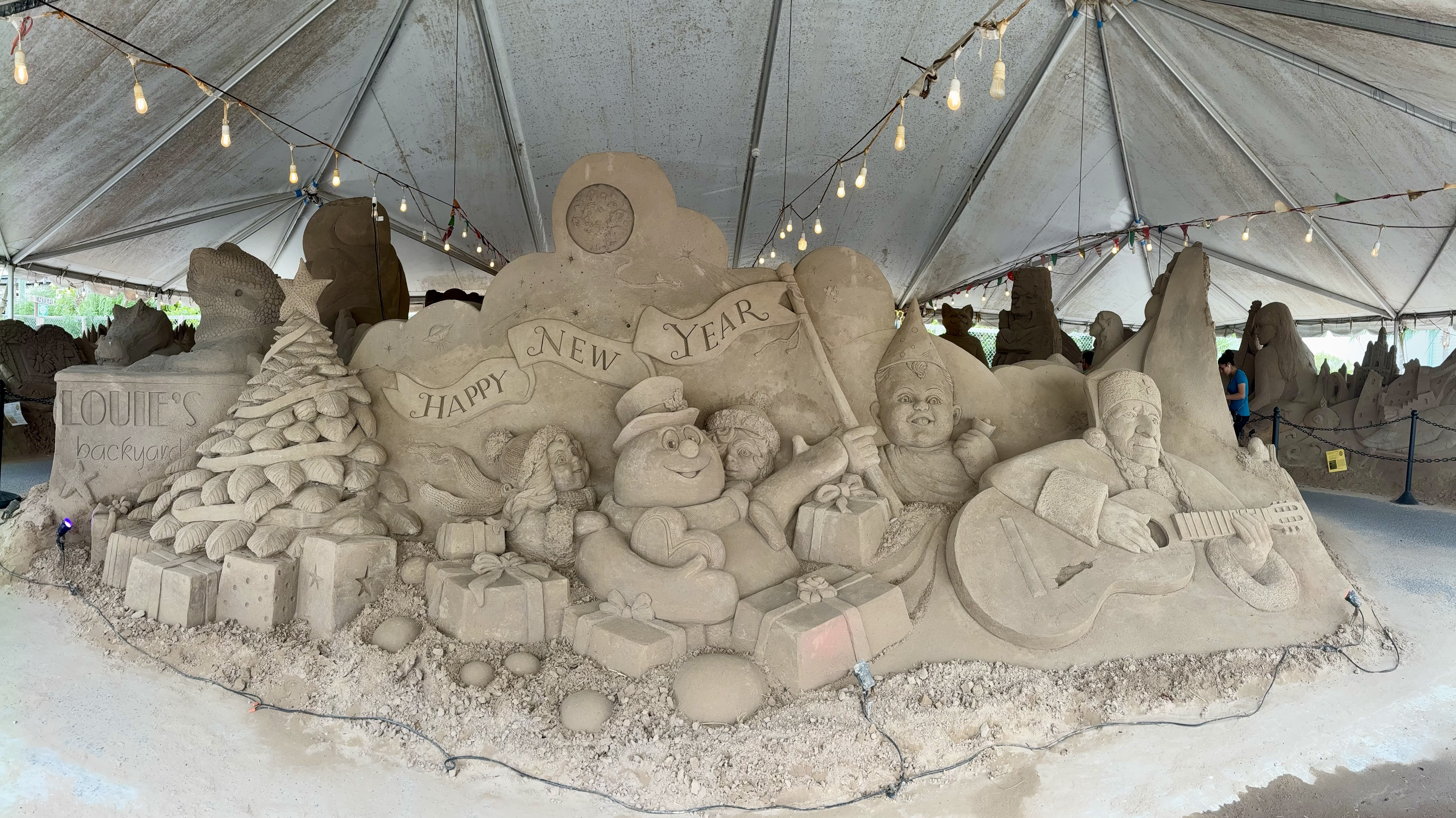 Holiday sand sculpture with a Christmas tree, snowman, gifts, and a Happy New Year banner