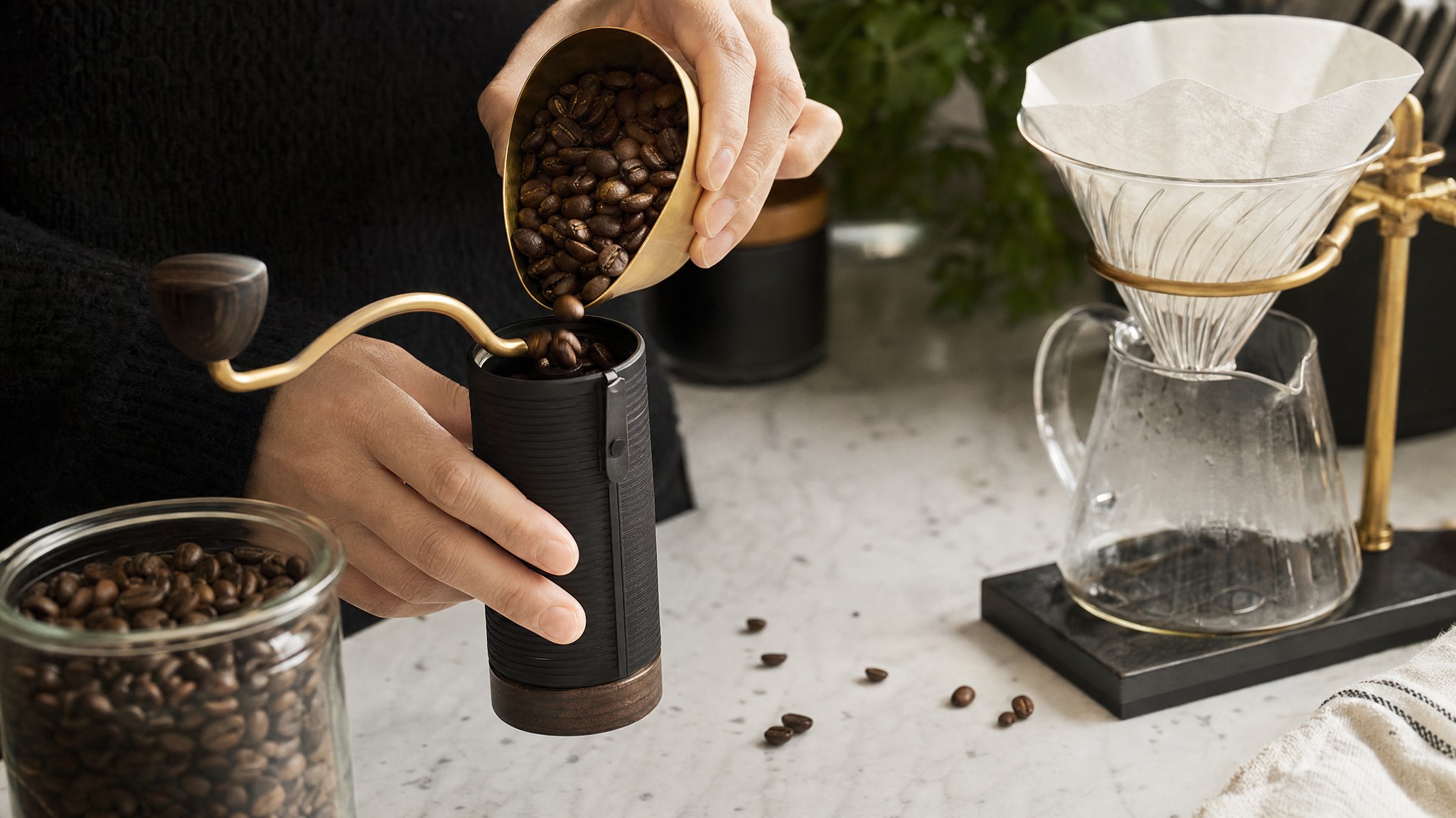 Whole coffee beans being measured into a hand grinder beside a pour-over brewer