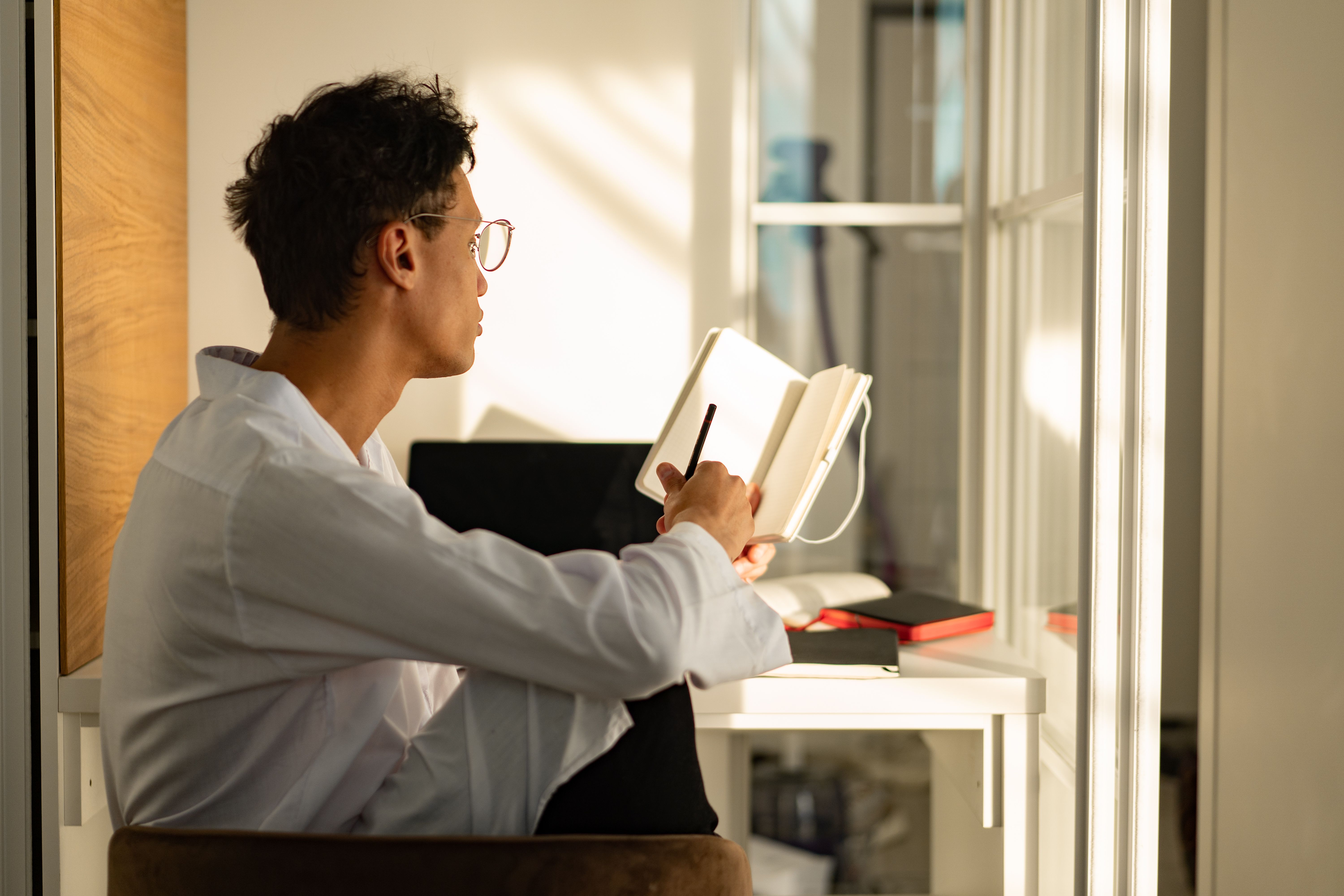Person writing in a notebook beside a sunny window