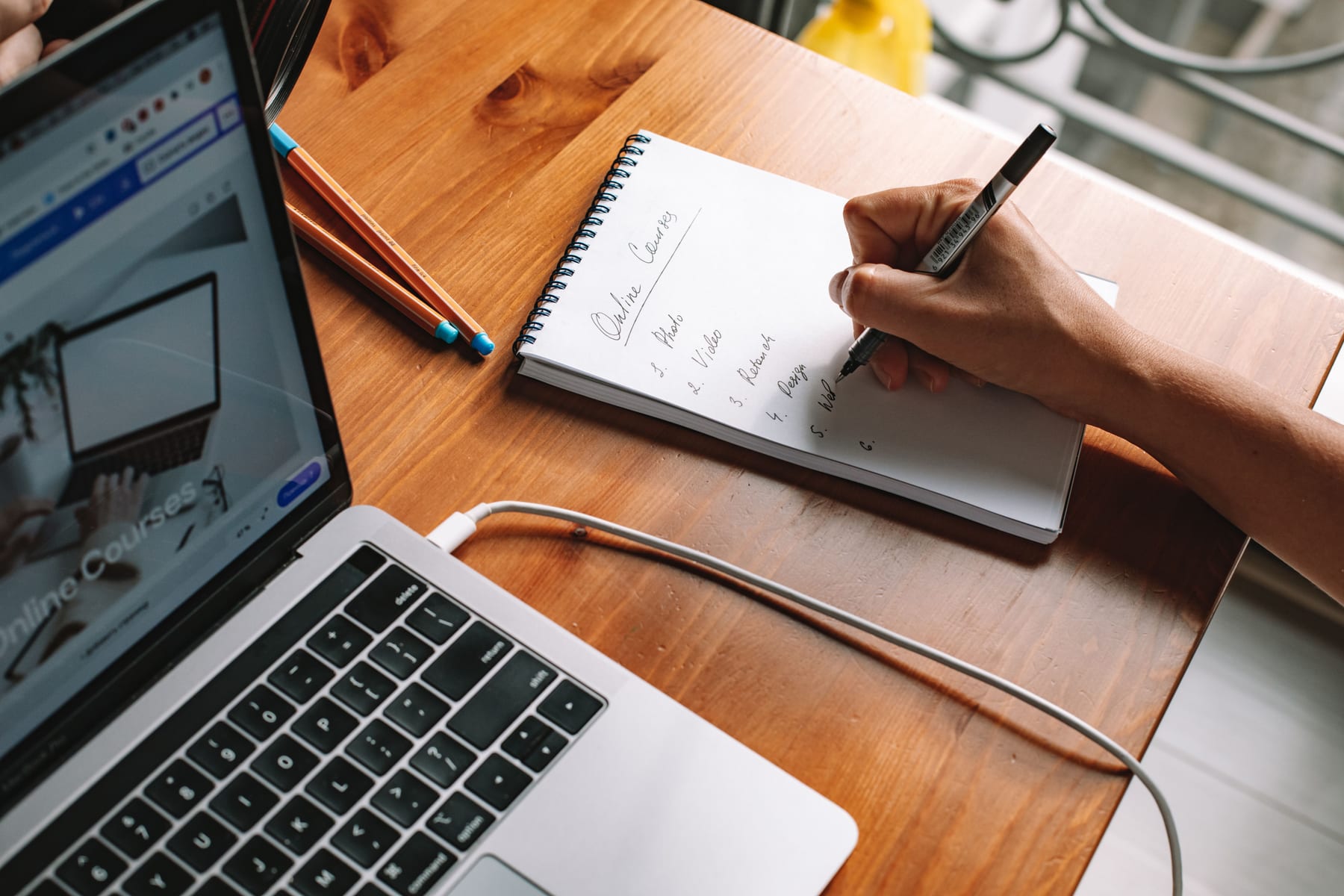 Person writing notes beside a laptop at a table