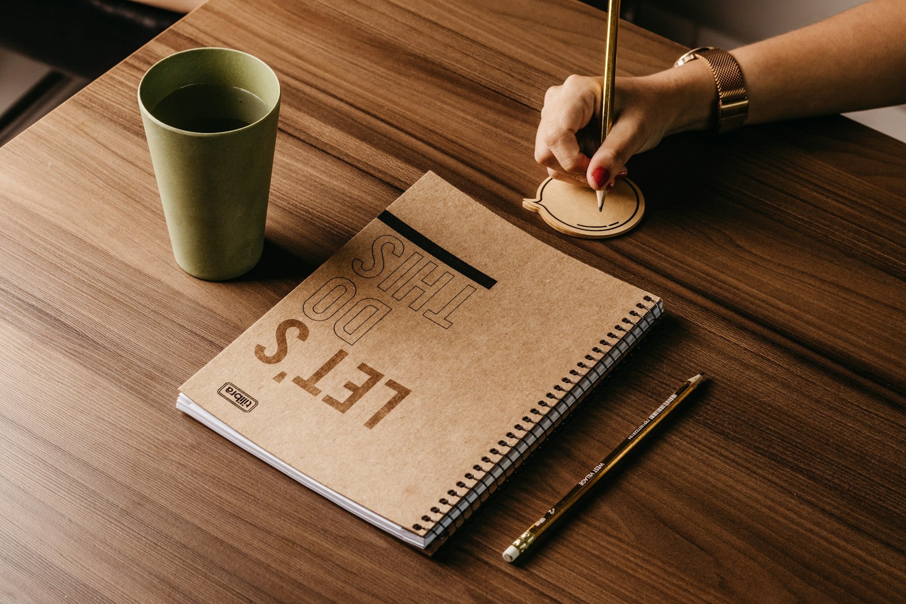 Person writing in a notebook beside a cup of coffee