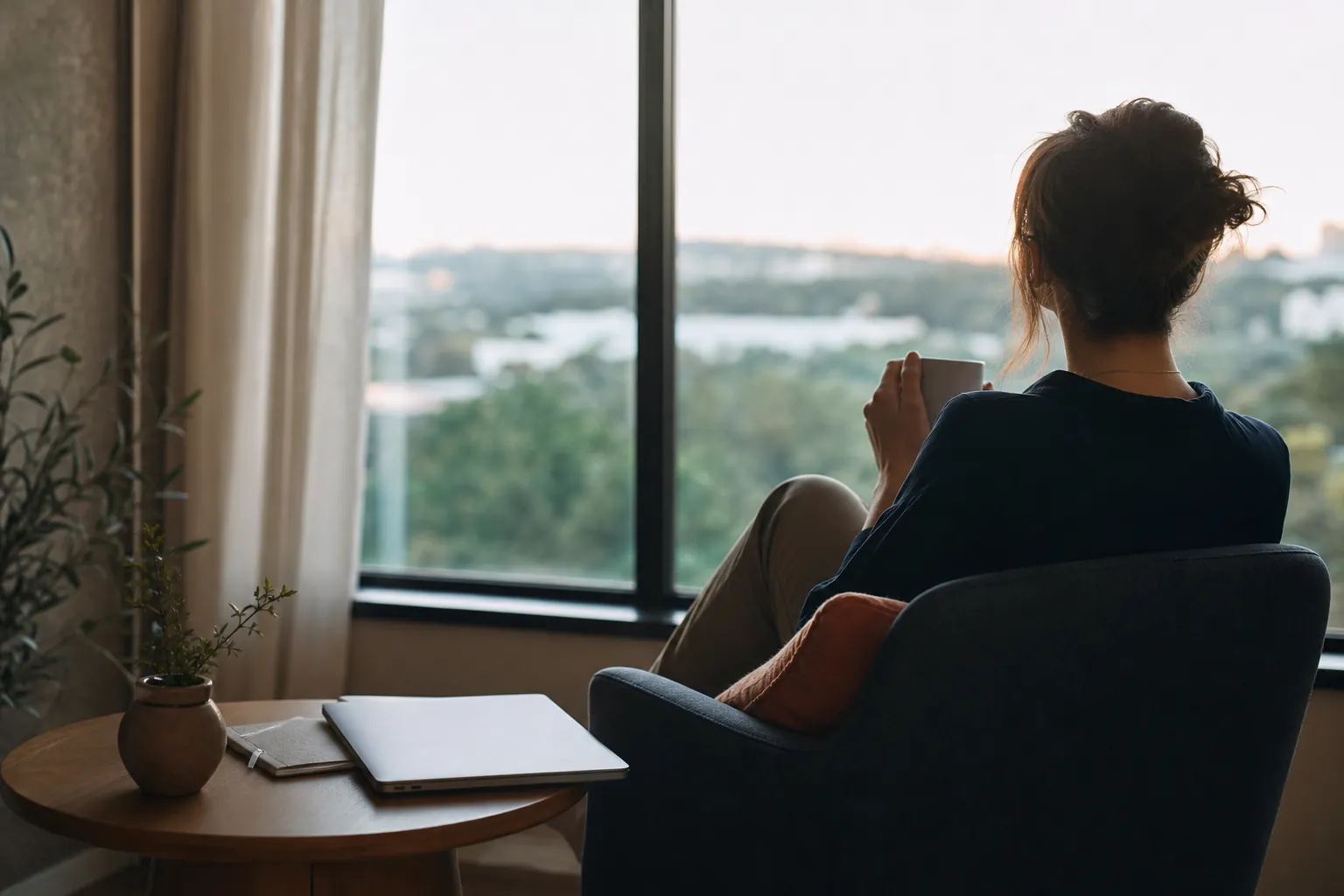 Person taking a quiet pause beside a window with a closed laptop nearby