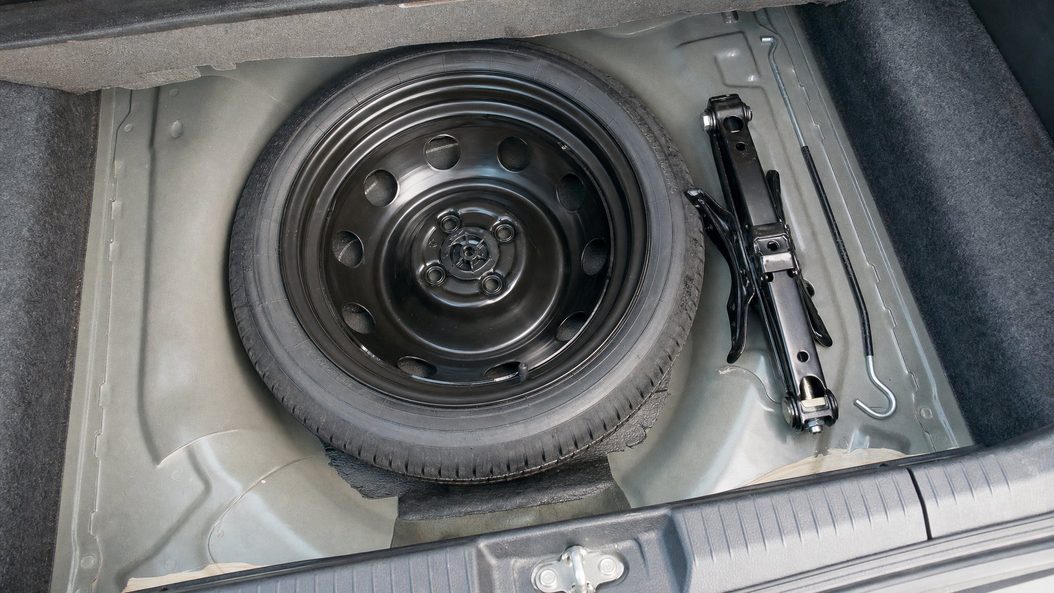 Temporary spare tire, vehicle jack, and lug wrench stored in a trunk compartment