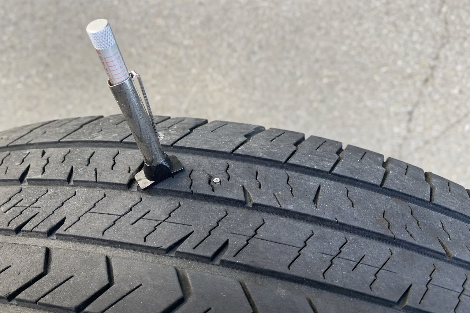 Tread-depth gauge next to a small puncture in the central tread of a tire