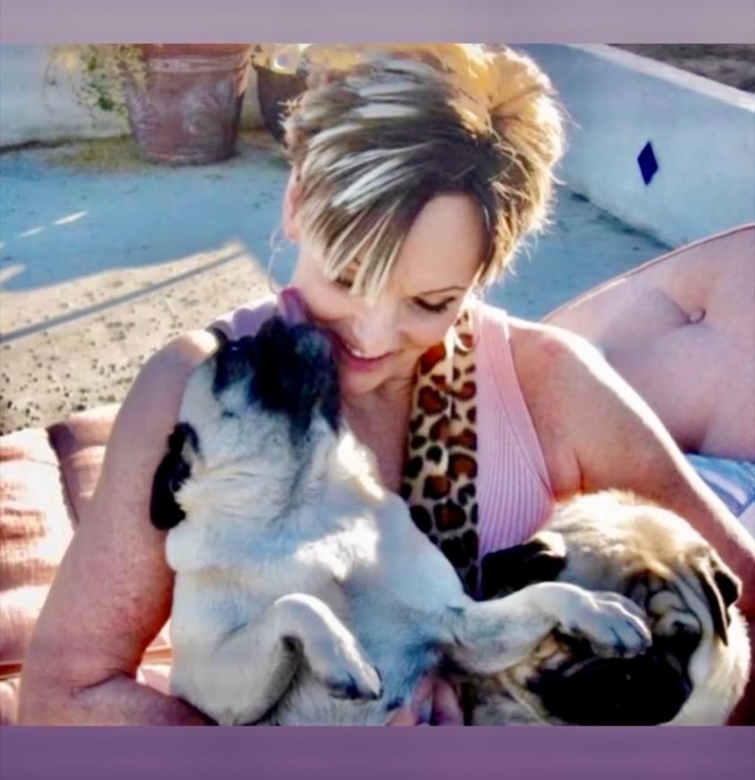 A woman cuddling two pugs outdoors