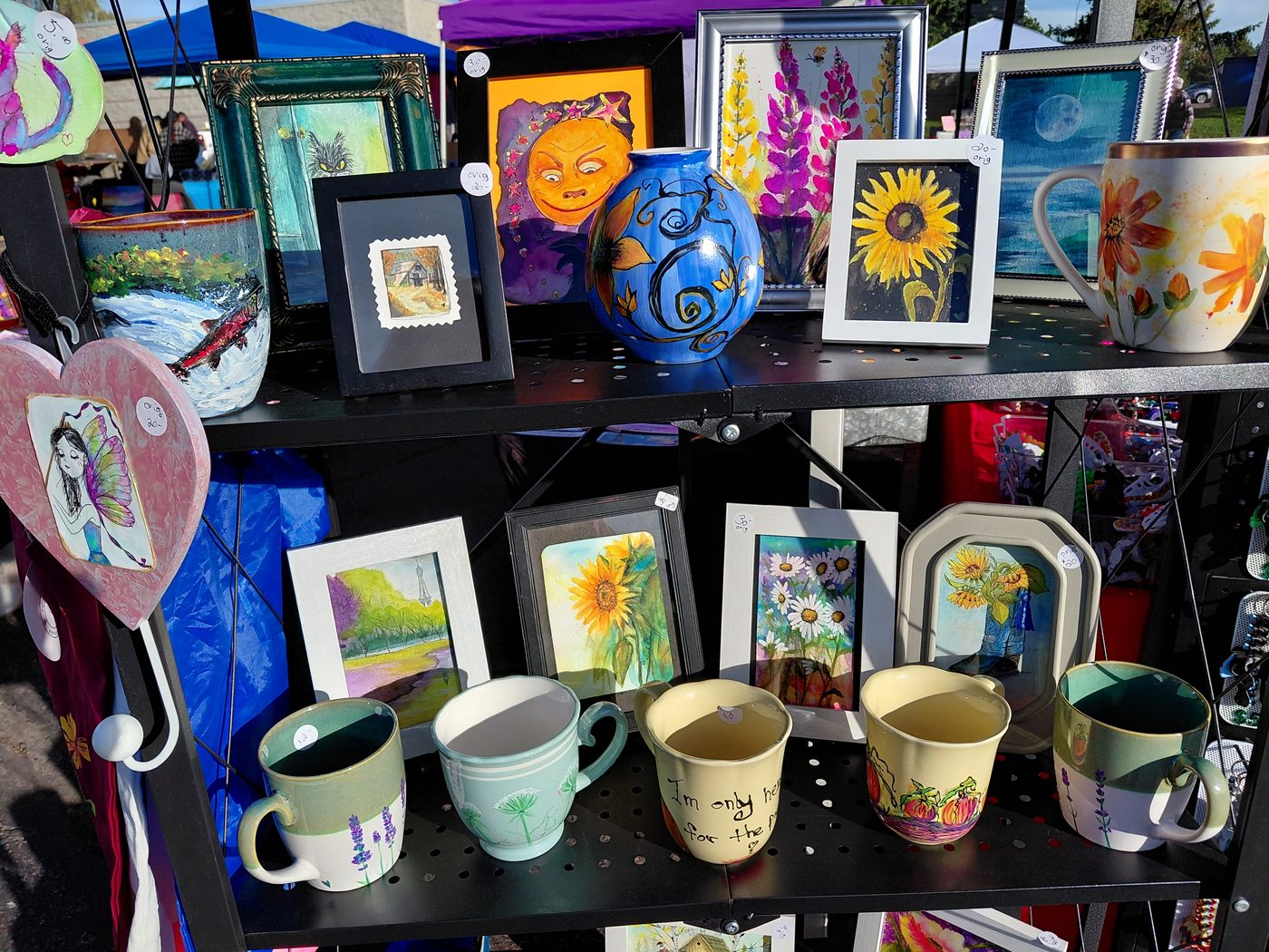 Colorful framed paintings, hand-painted mugs and glassware at Deahn’s market stall