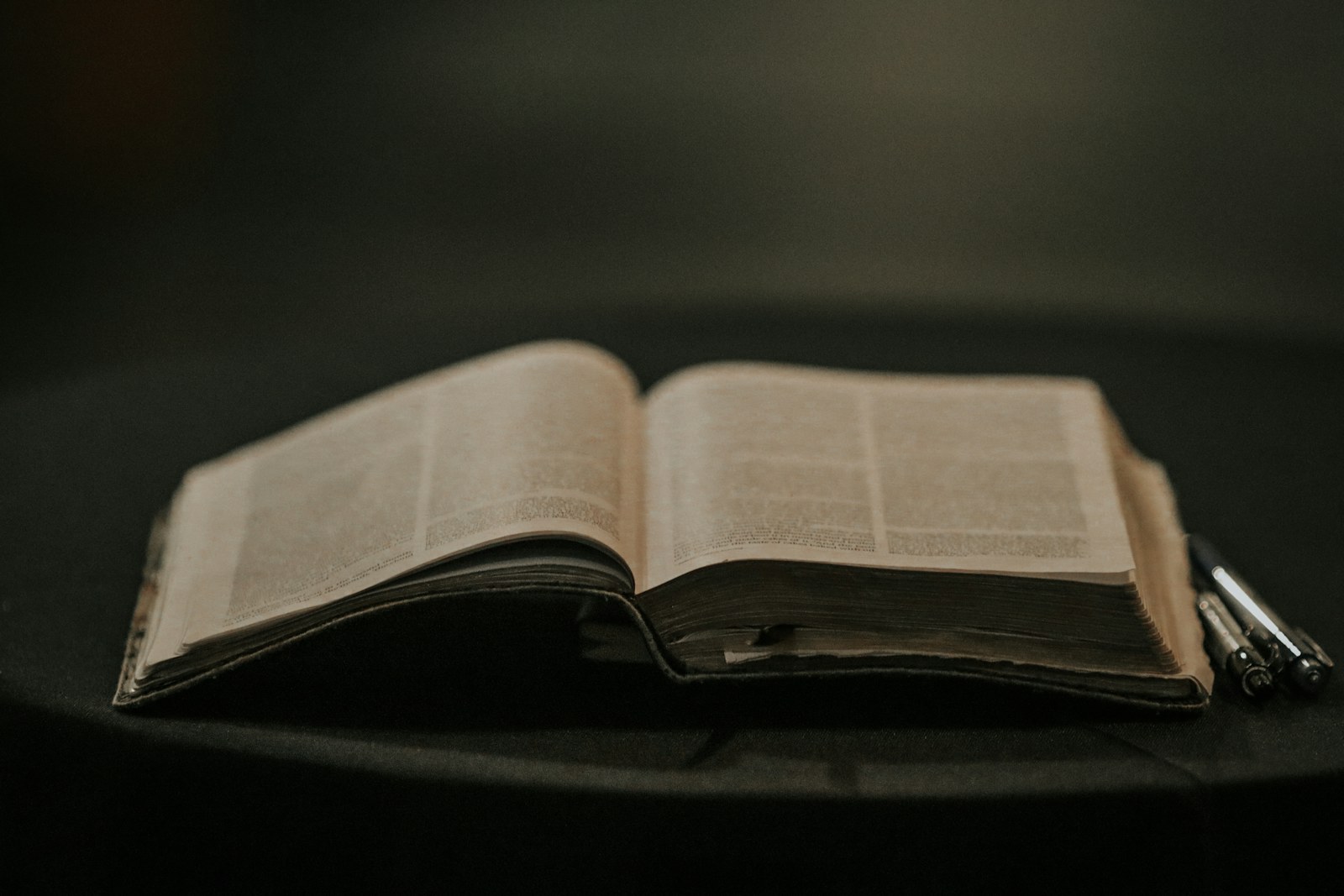 Open Bible and pens in a quiet, dim room