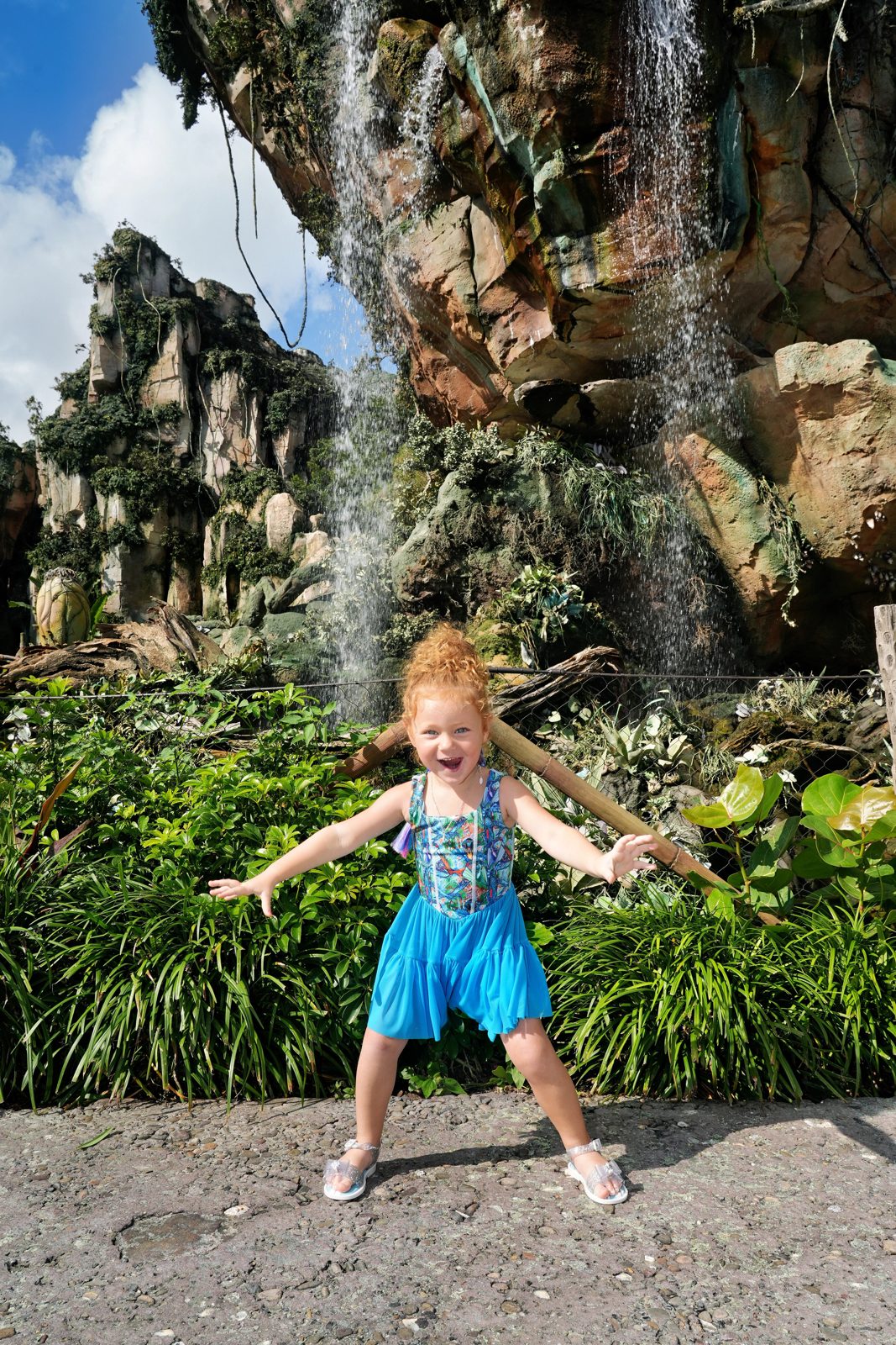 Londyn smiling in a bright blue dress in front of a waterfall