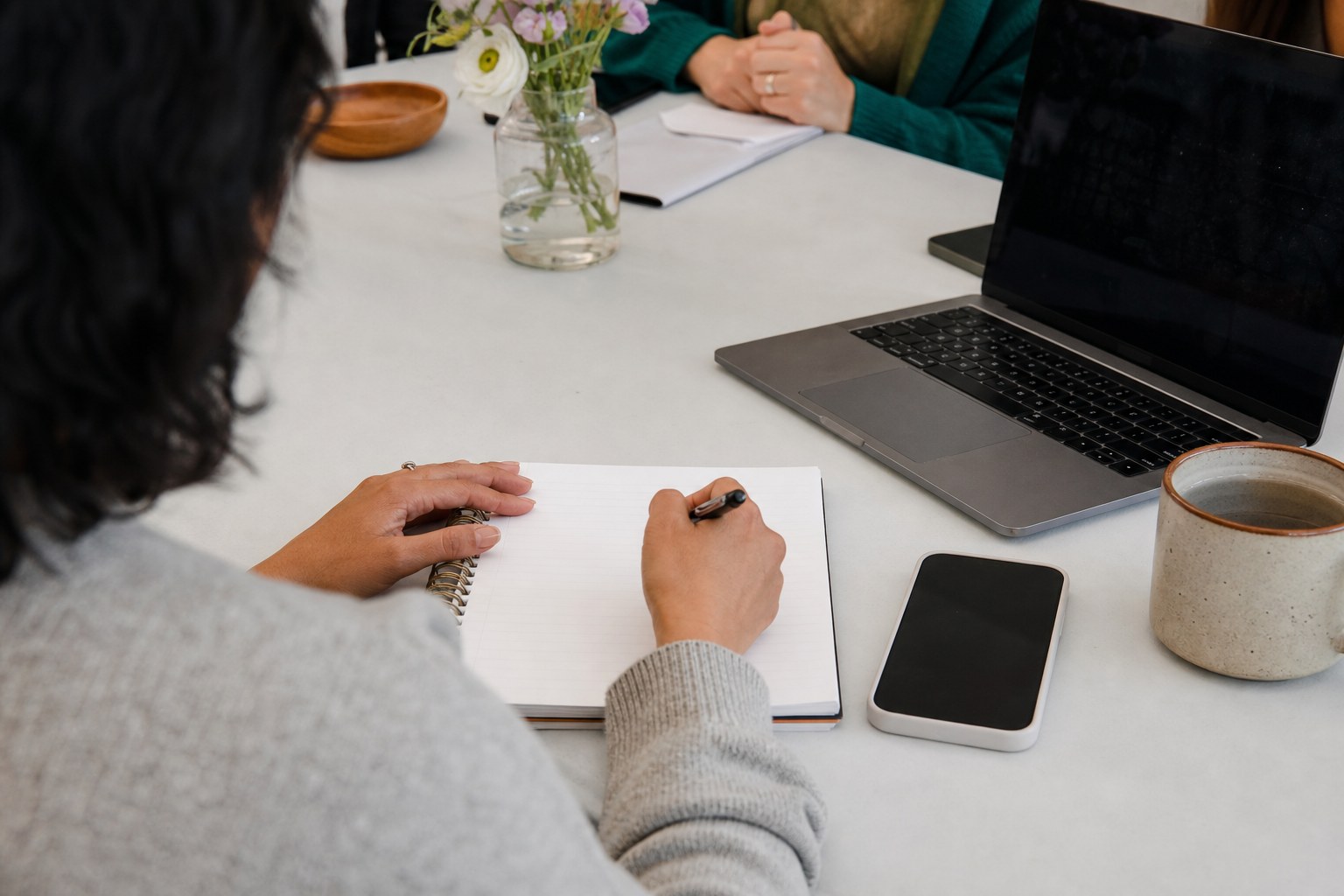 Person writing down online safety steps beside a laptop and phone