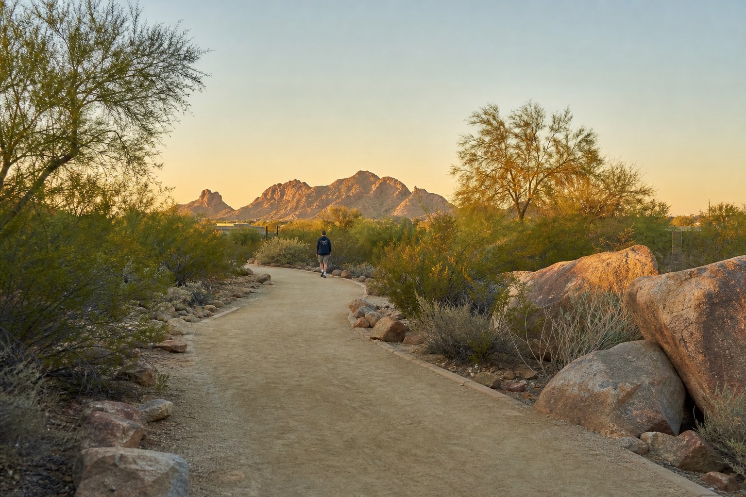 A person walking along a quiet desert path at sunset