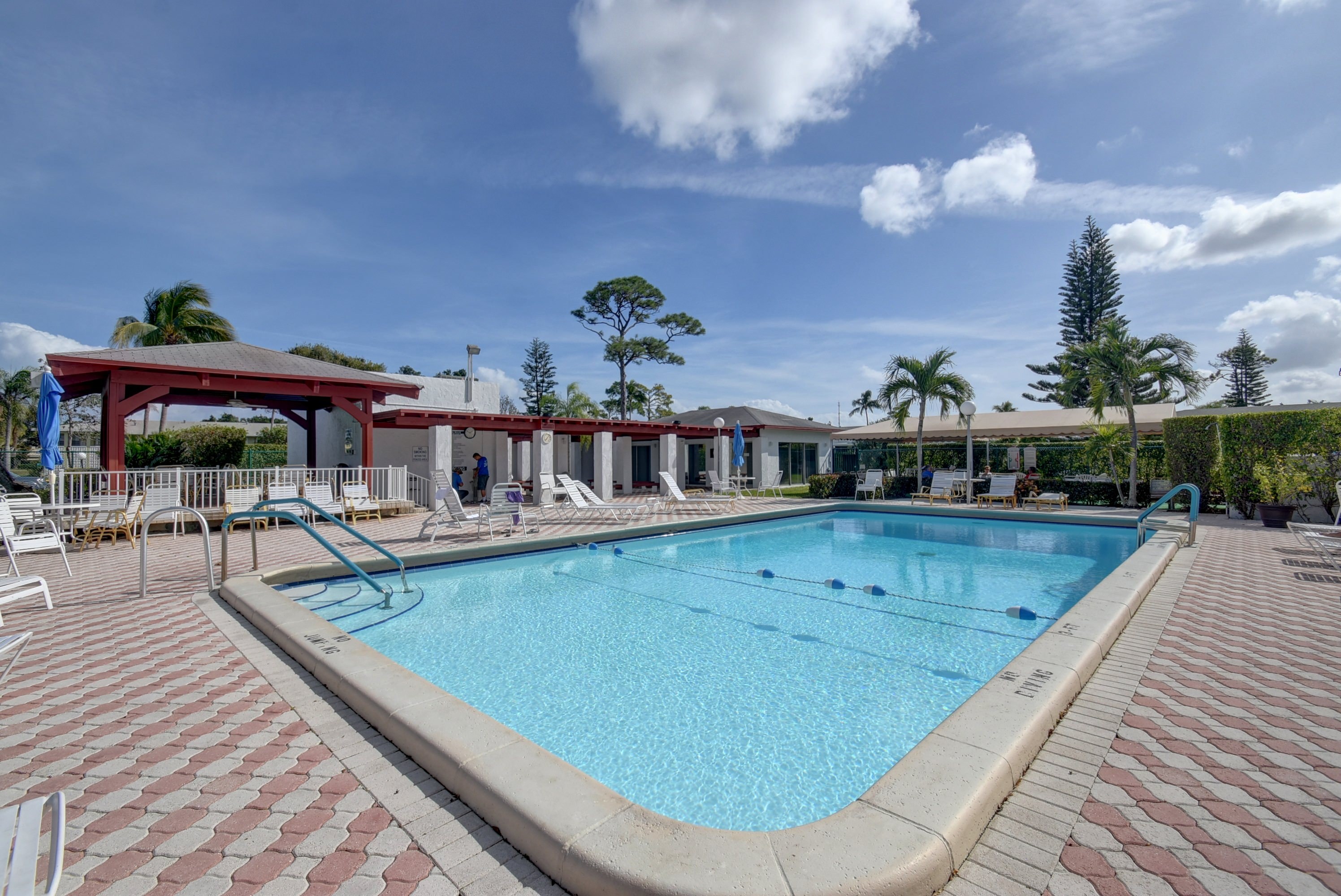 Pines of Delray outdoor swimming pool with lounge chairs and clubhouse spaces