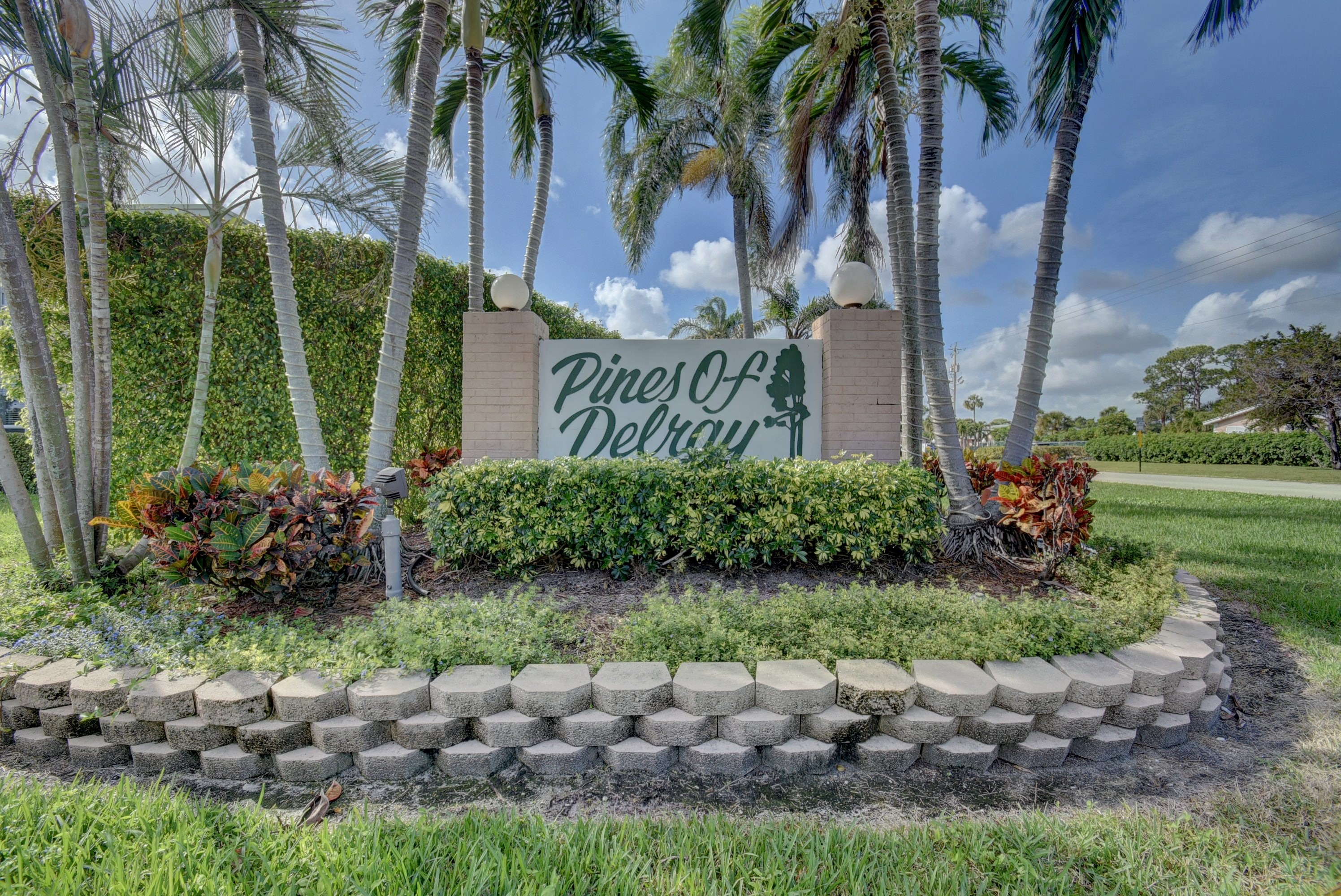 Pines of Delray entrance sign framed by palm trees and tropical landscaping in Delray Beach