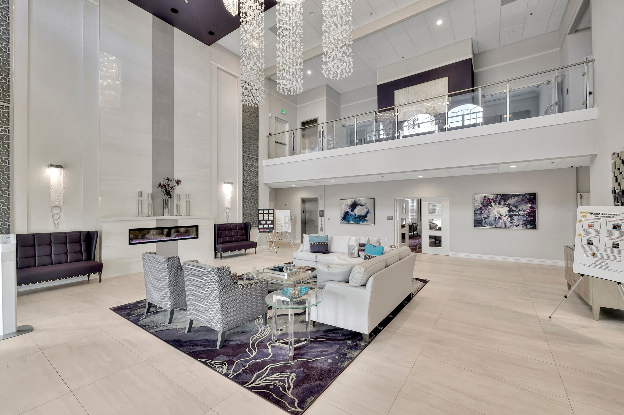 Two-story Majestic Isles clubhouse lounge with seating, chandeliers, and bright arched windows