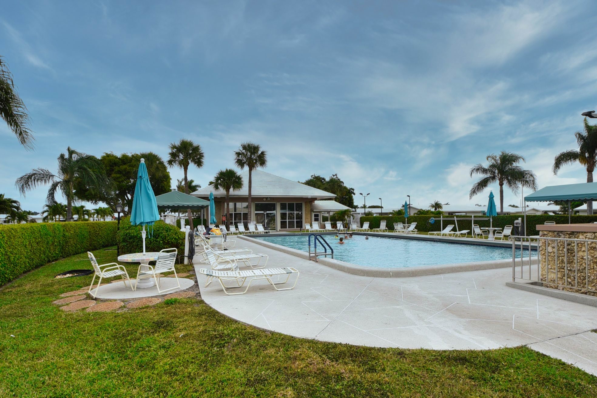 Outdoor swimming pool with lounge chairs, palms, and clubhouse at Palm Beach Leisureville