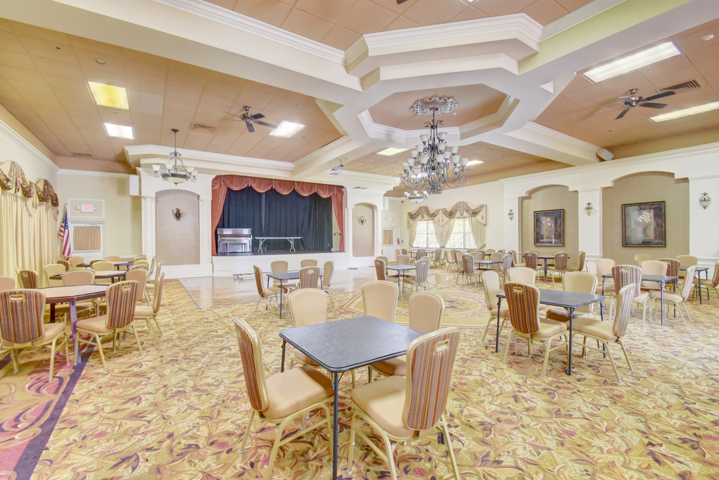 Palm Chase Lakes clubhouse gathering room set with dining tables, chandeliers, and a raised stage