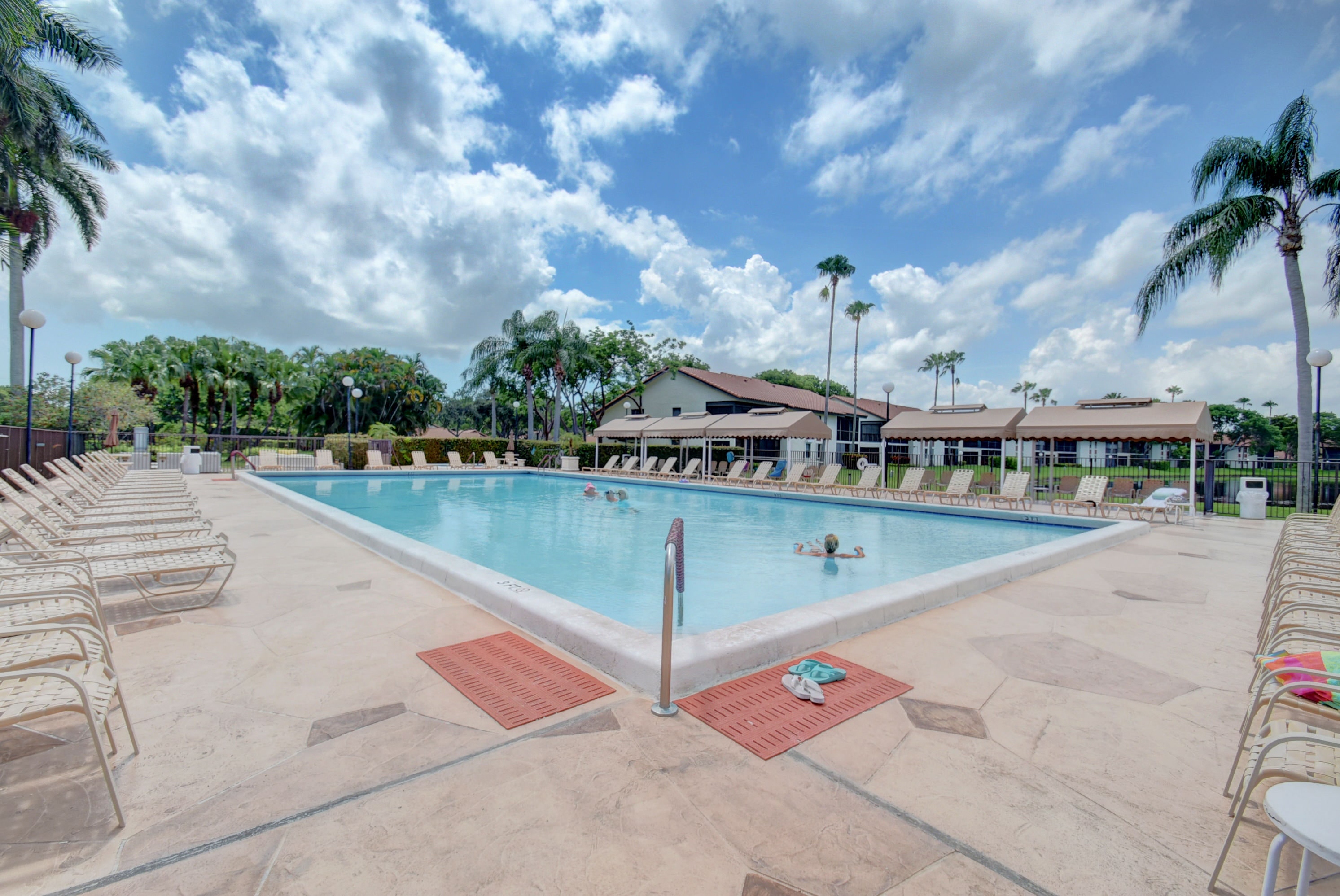 Palm Chase Lakes outdoor swimming pool with lounge chairs, palms, and clubhouse in the background
