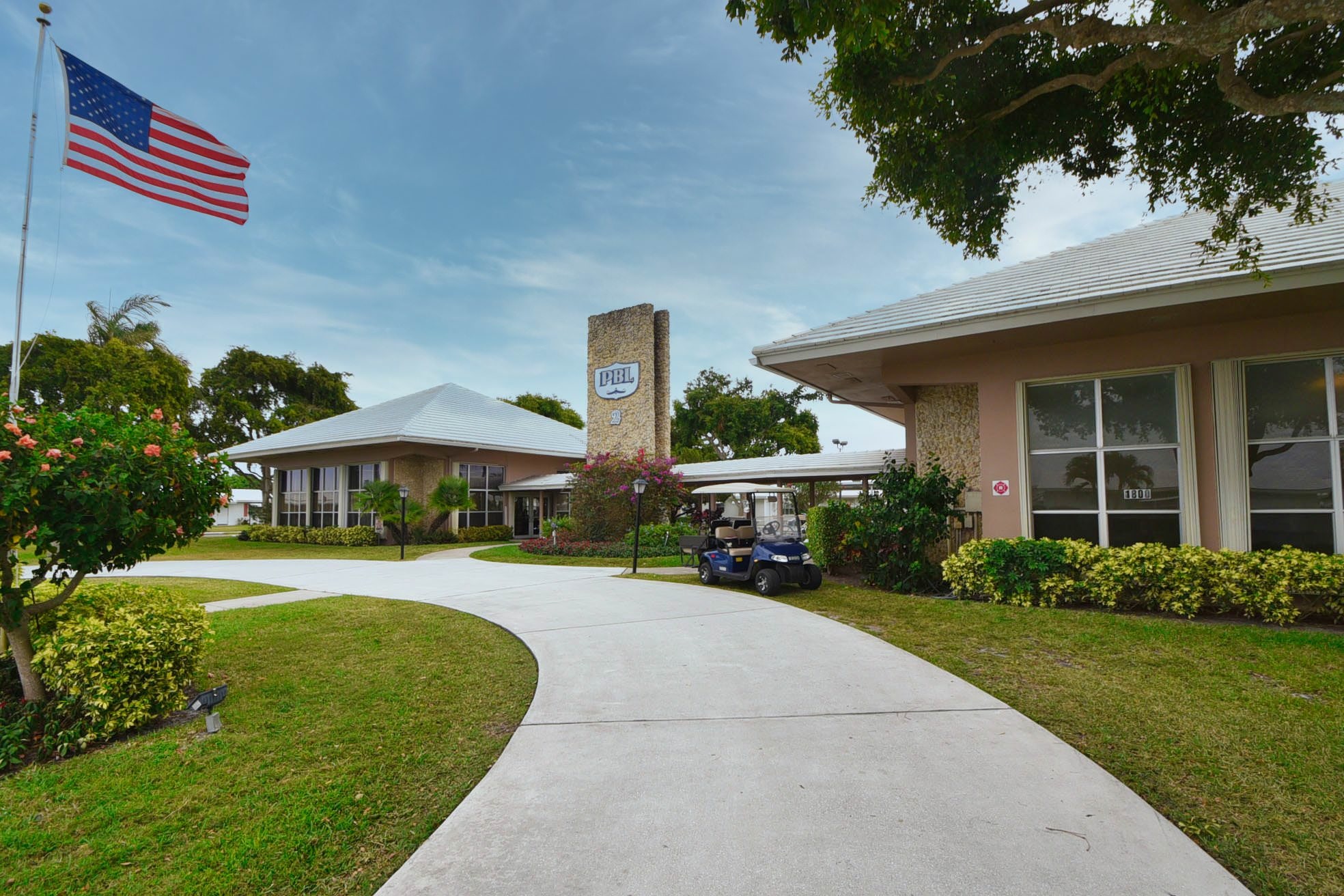 Palm Beach Leisureville clubhouse entrance with community sign, landscaped walkway, and golf cart