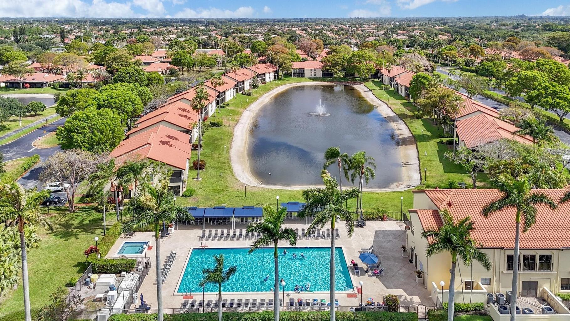 Aerial view of the Palm Chase Lakes clubhouse, resort-style pool, palms, and lakeside homes