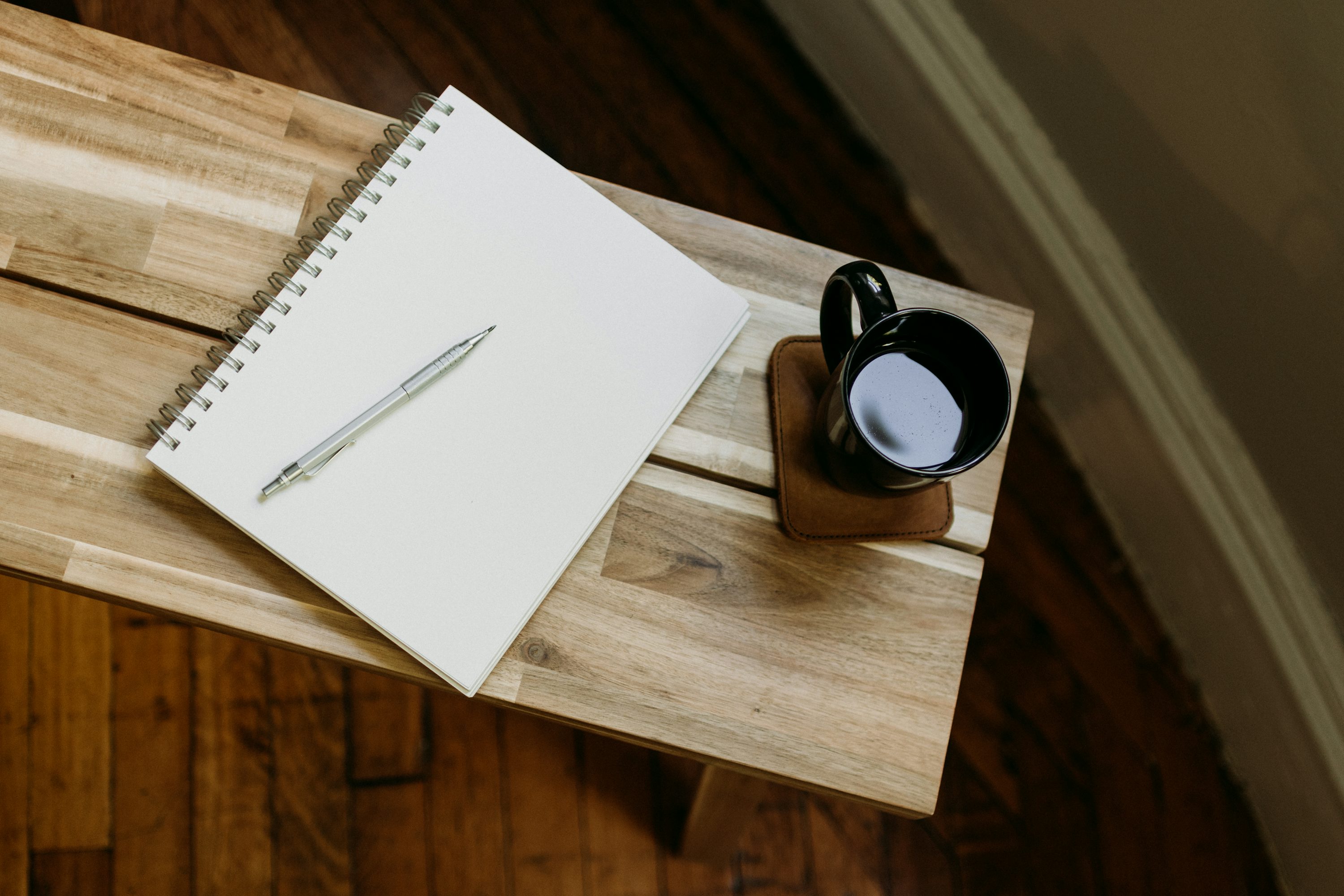 Coffee cup and pen beside a book on a wooden table