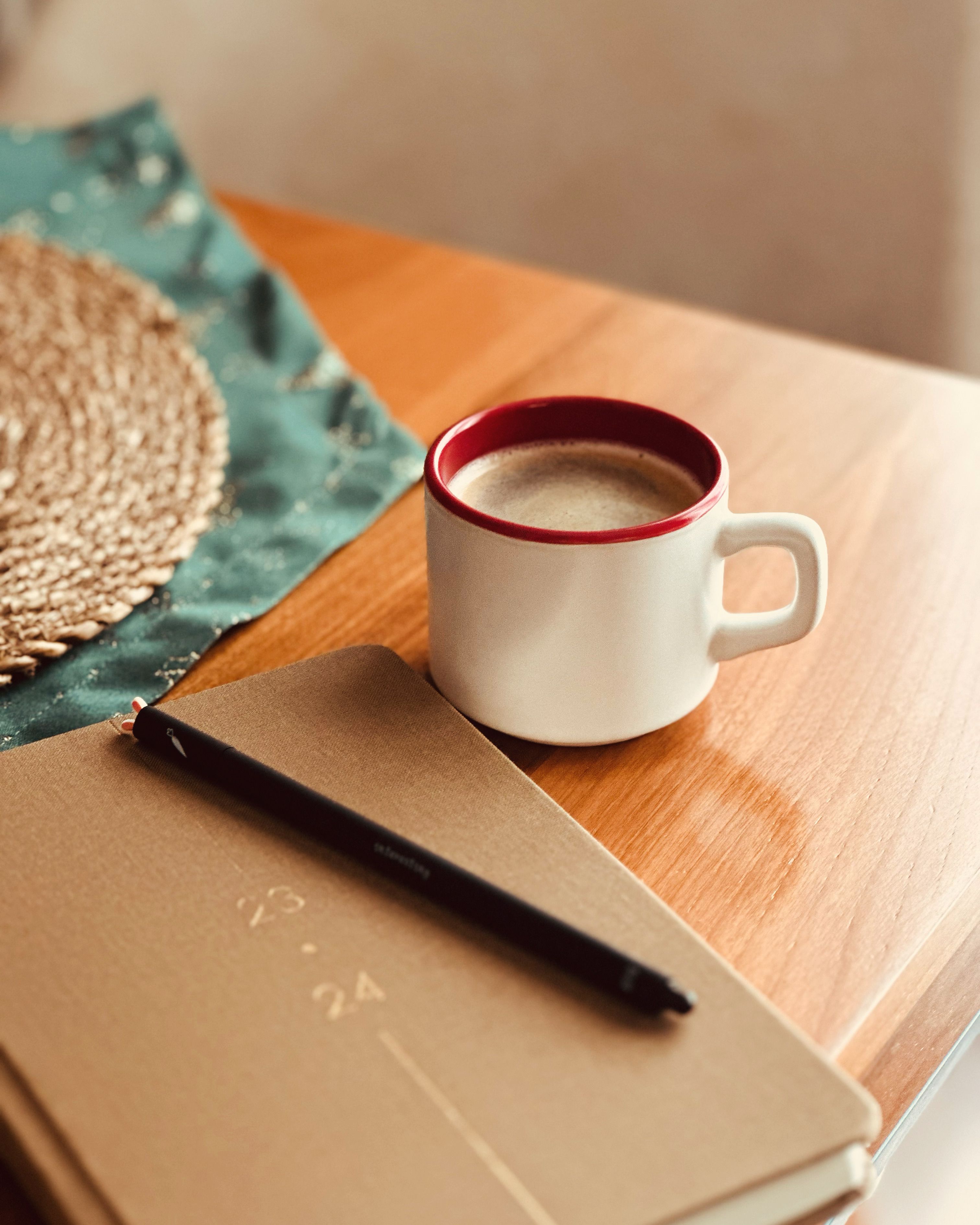 Coffee mug, notebook, and pen on a warm wooden table