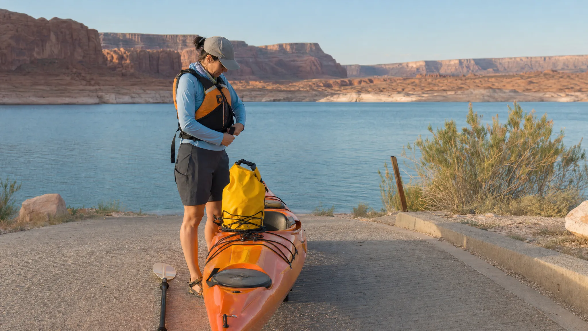A kayaker checking a life jacket and dry bag beside a Lake Powell launch ramp
