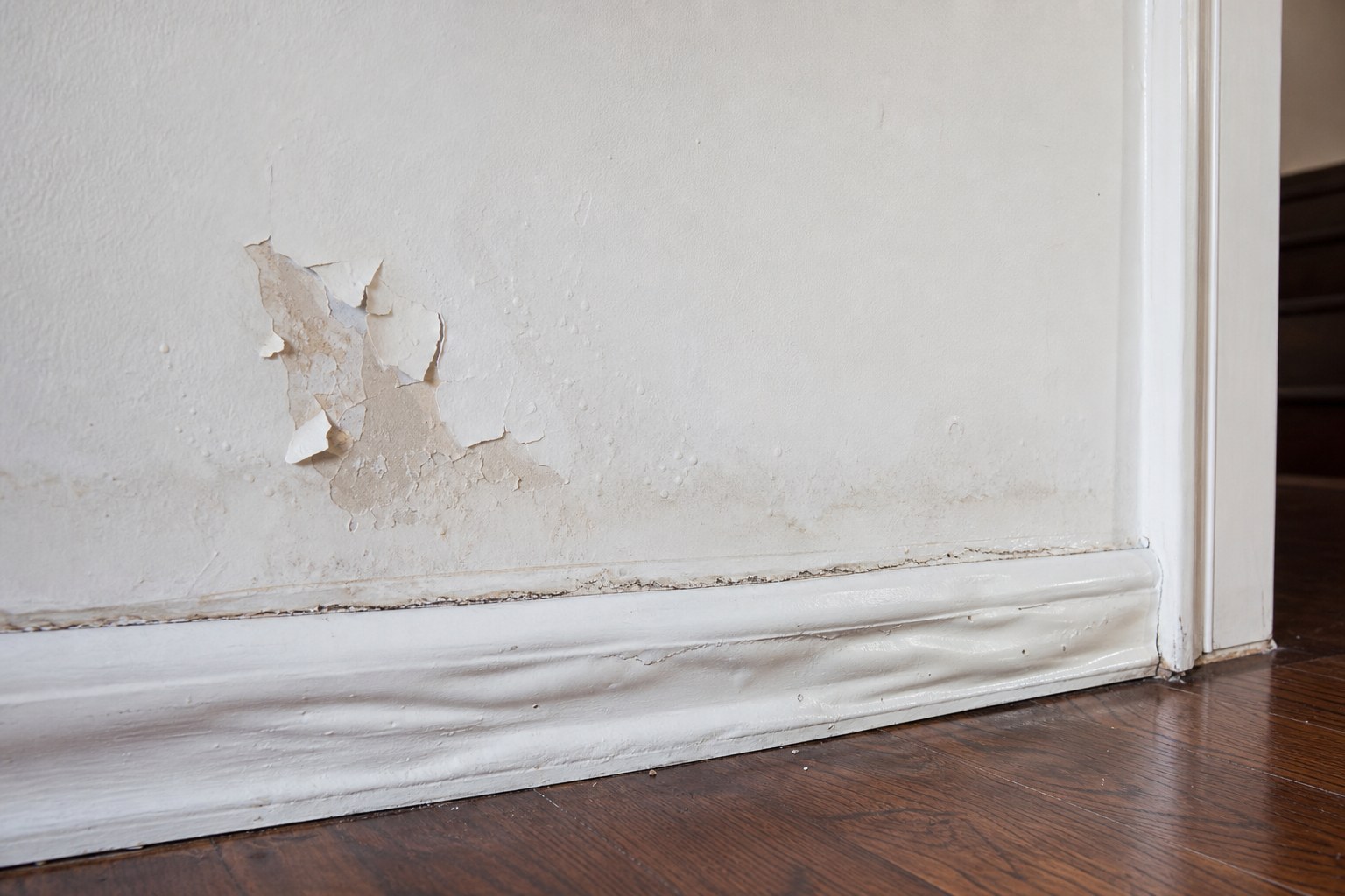 Peeling wall paint and swollen baseboard showing signs of moisture damage