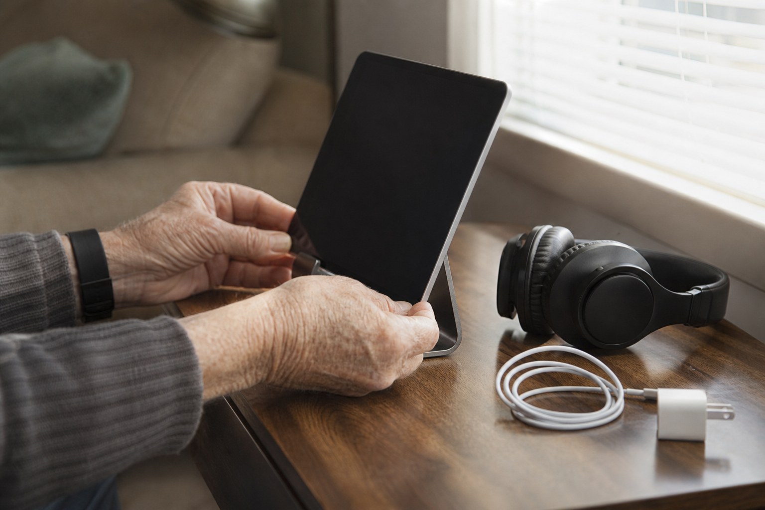 Hands setting up a tablet, headphones, and charger before a video visit