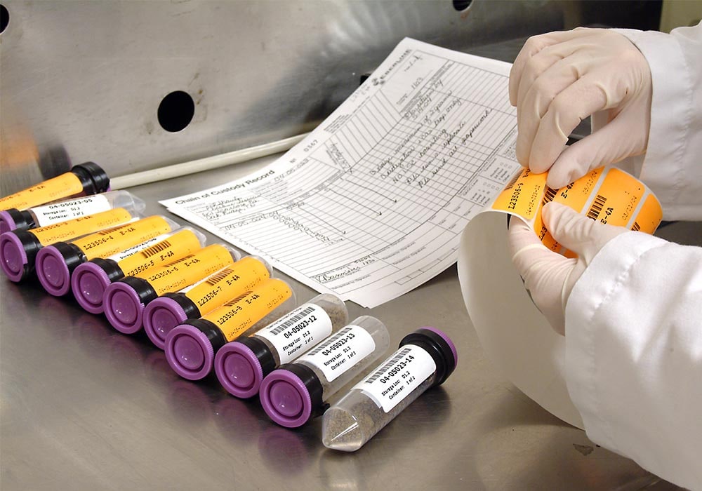 Technician applying sample labels to laboratory vials beside a chain-of-custody record