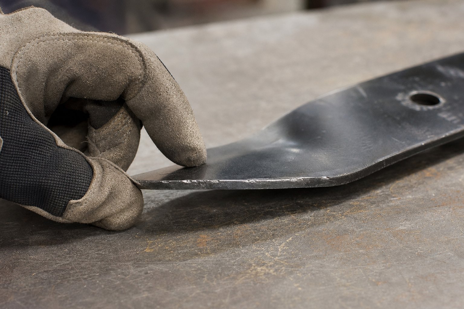 Gloved hand inspecting wear along a removed rotary mower blade