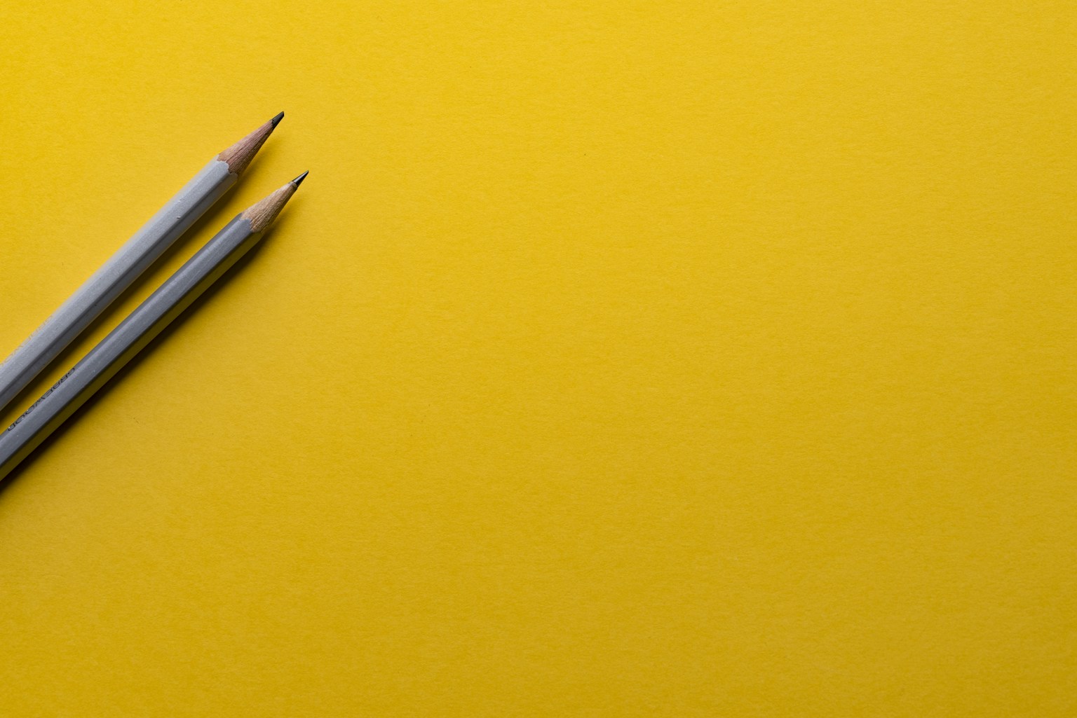 Two sharpened pencils on a bright yellow writing surface