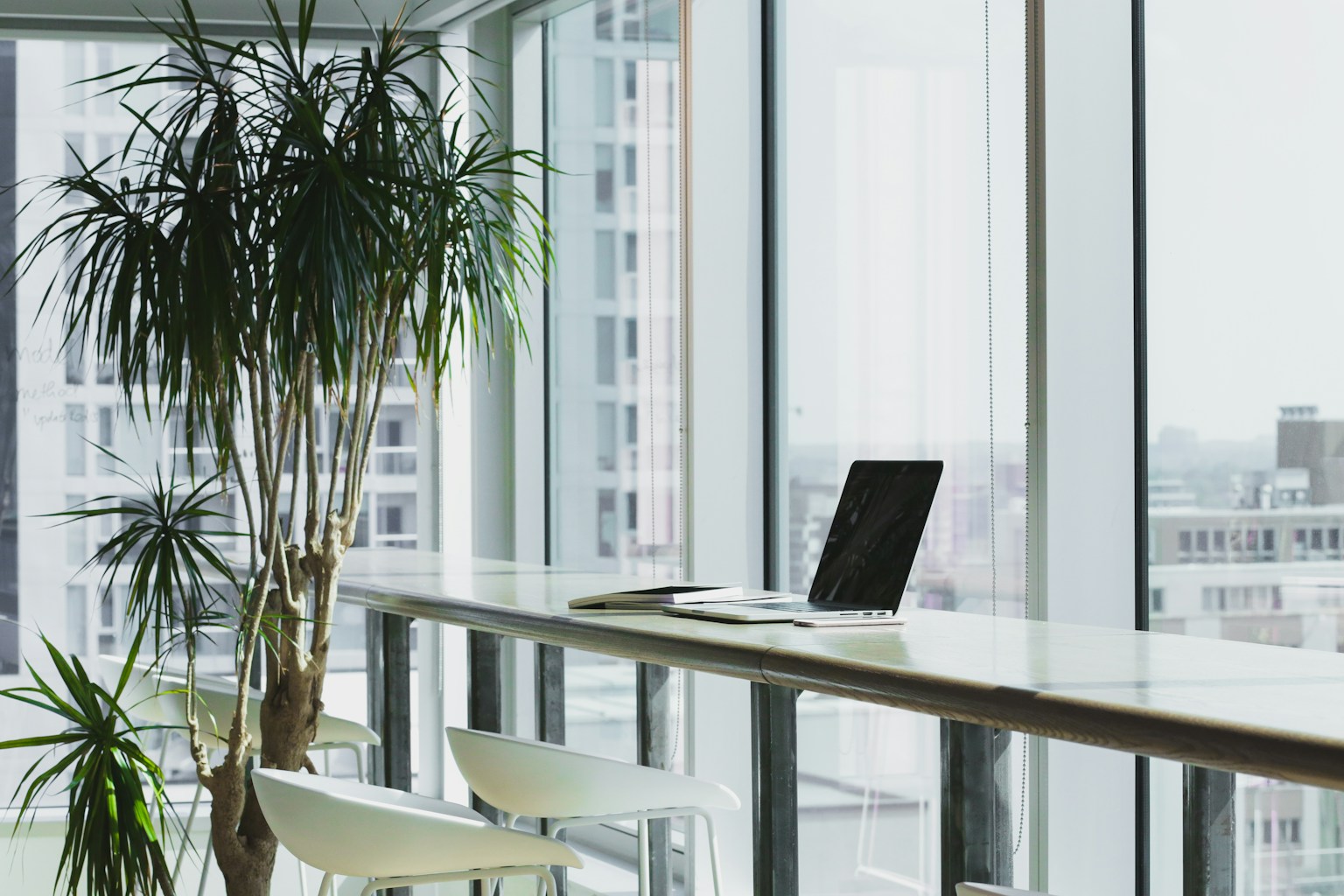 A quiet desk beside tall windows with a notebook and laptop