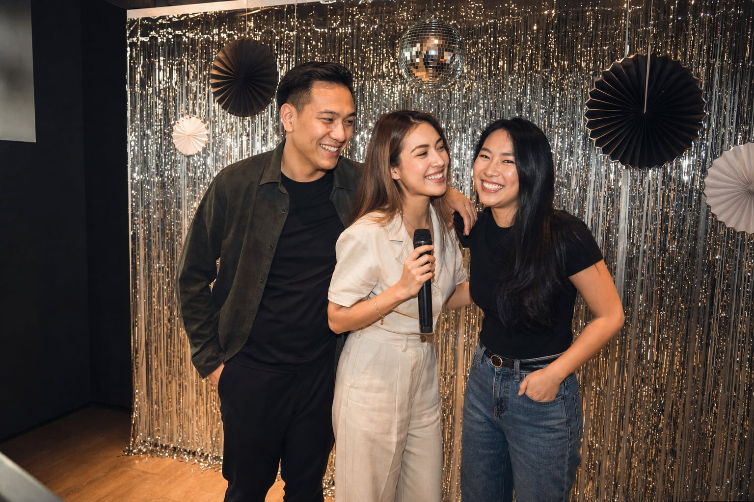 Three friends posing with a microphone at a metallic karaoke party backdrop