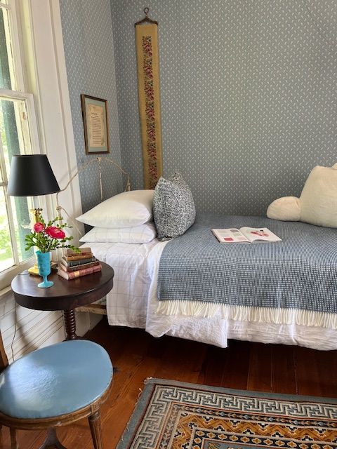 A guest bed with a blue coverlet beside a window