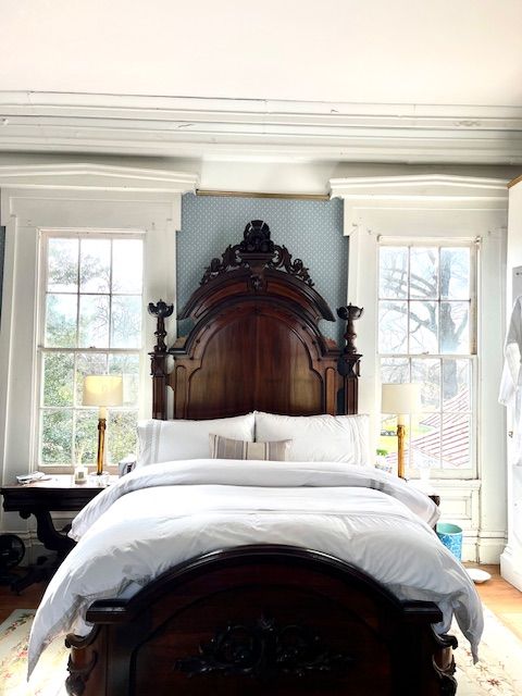 An antique wooden bed between two windows