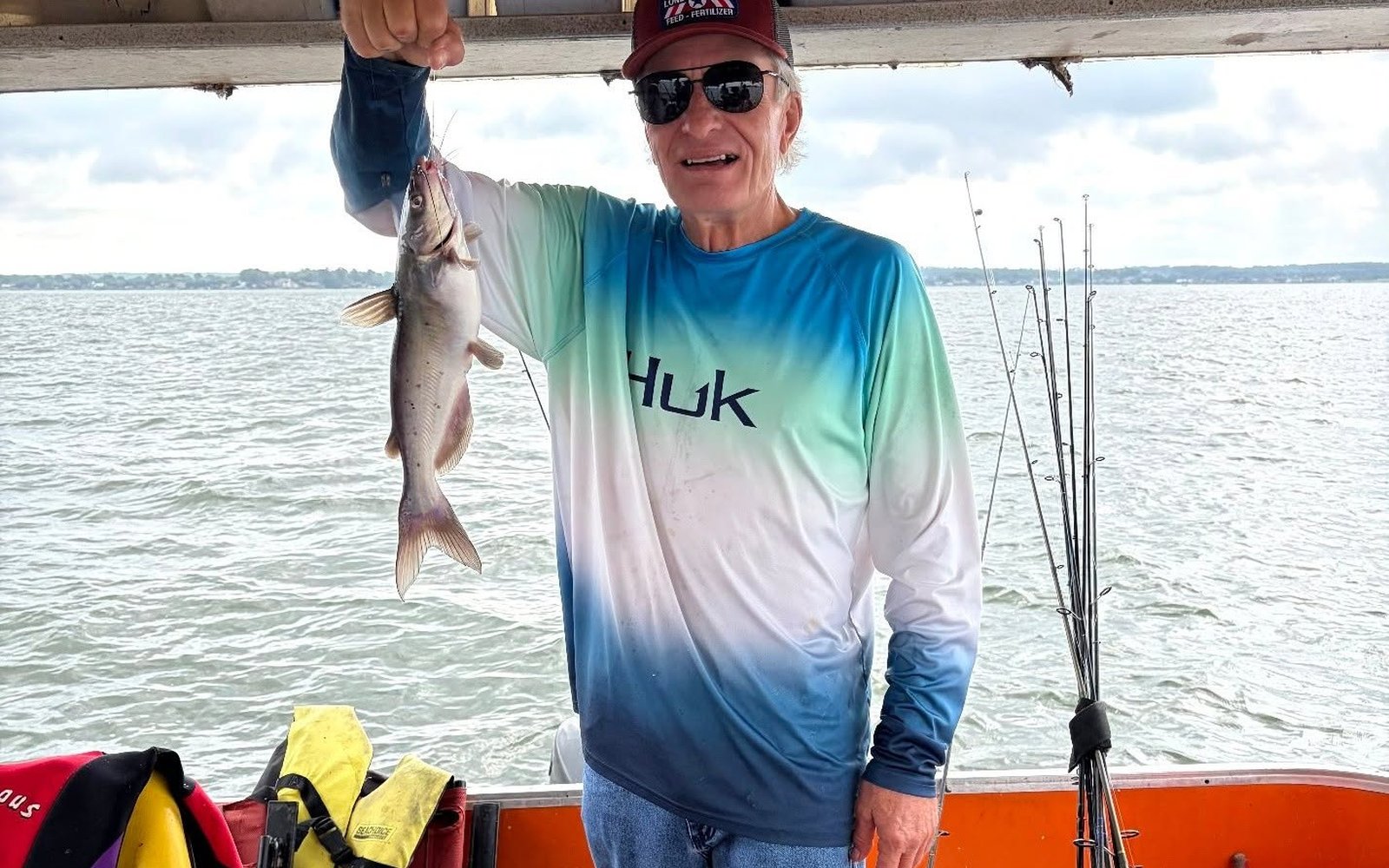 Billy Mills holding a catfish beside fishing rods on a Lake Conroe boat. Lake Conroe Fishing Guide - Billy Mills