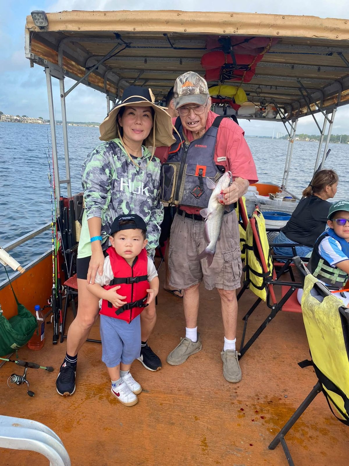 A child in a red life jacket with family and Billy holding a catfish